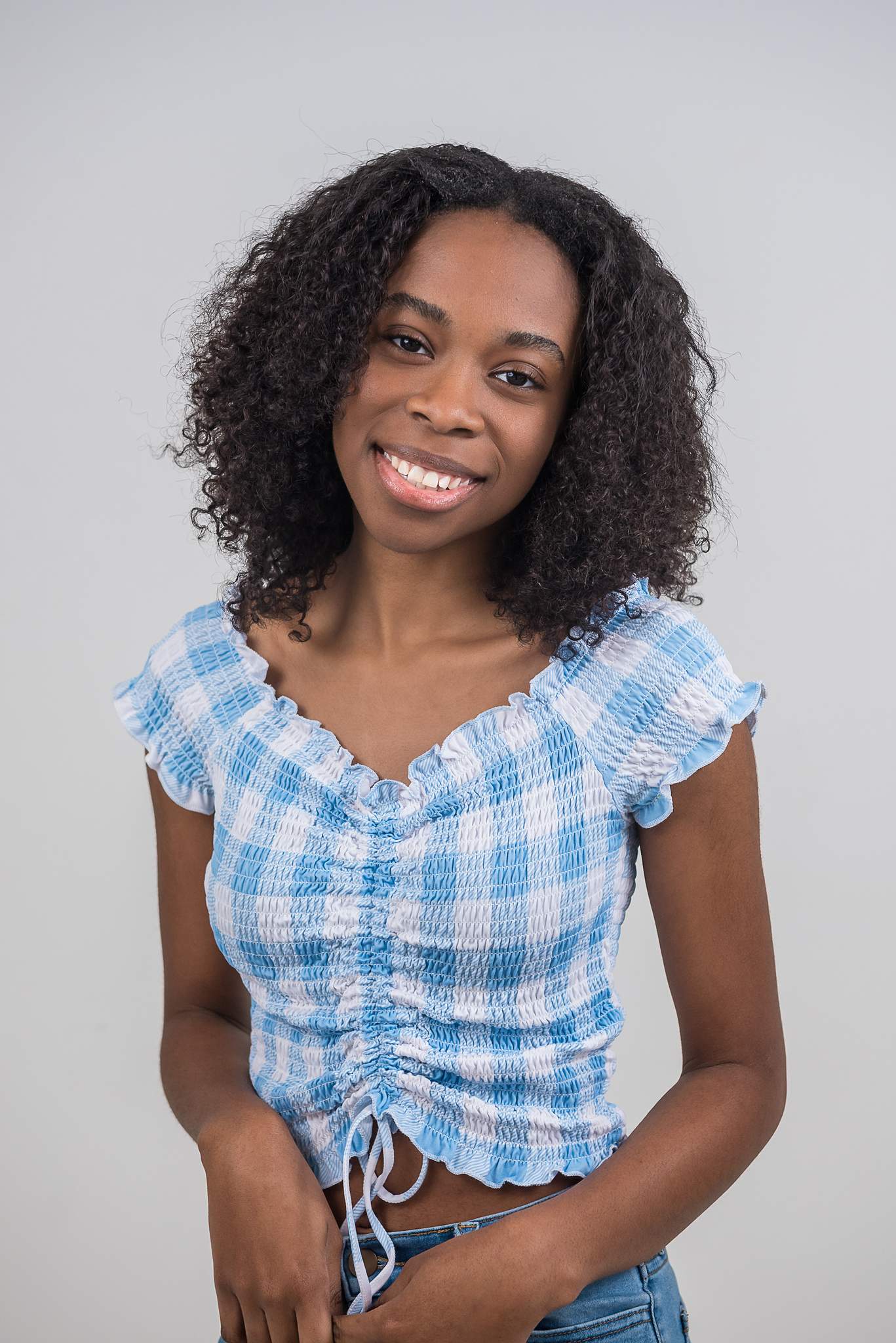 Woman smiling in a blue gingham top in natural window light at White Wall Studio