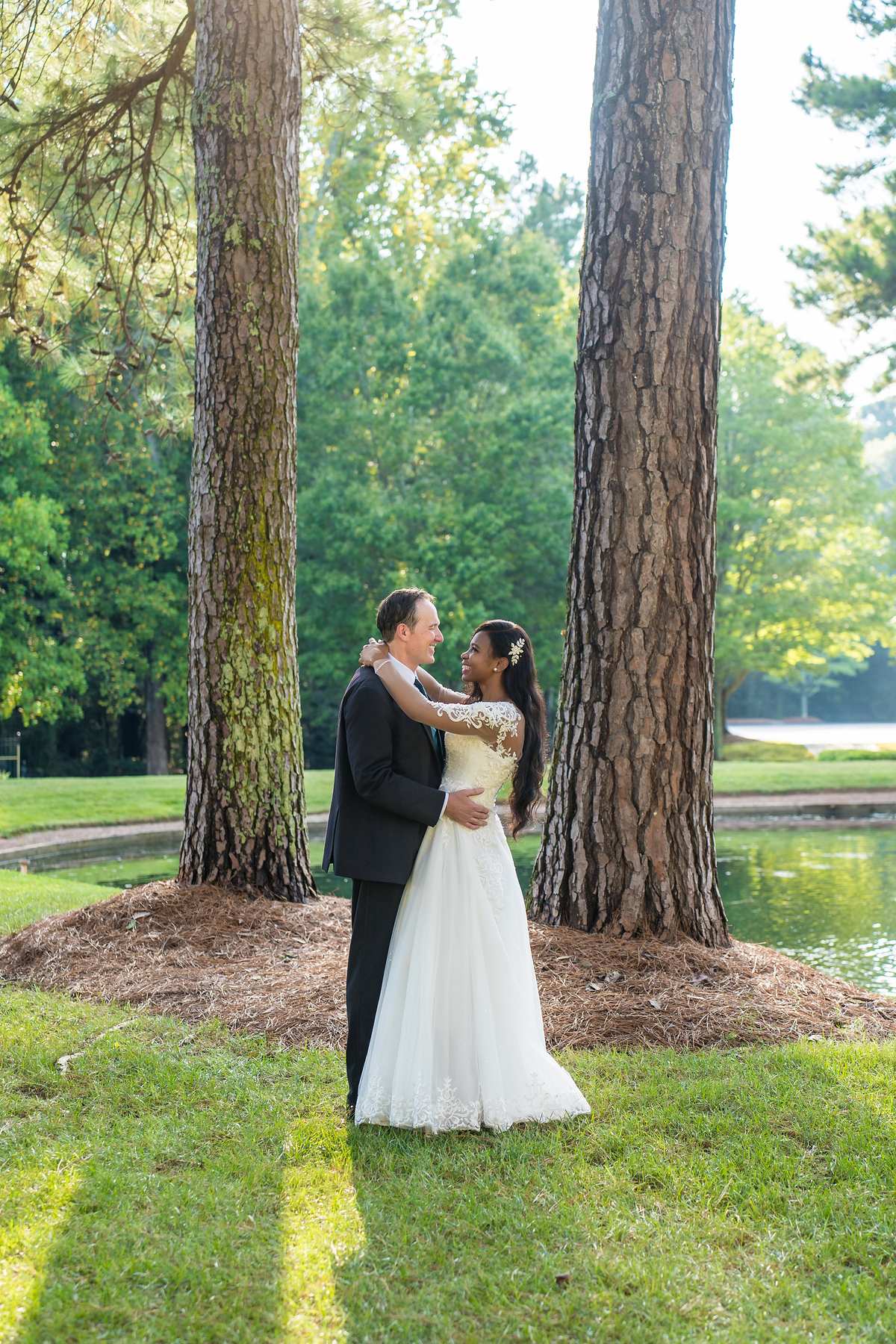 Interracial couple embracing between tall pine trees after their wedding