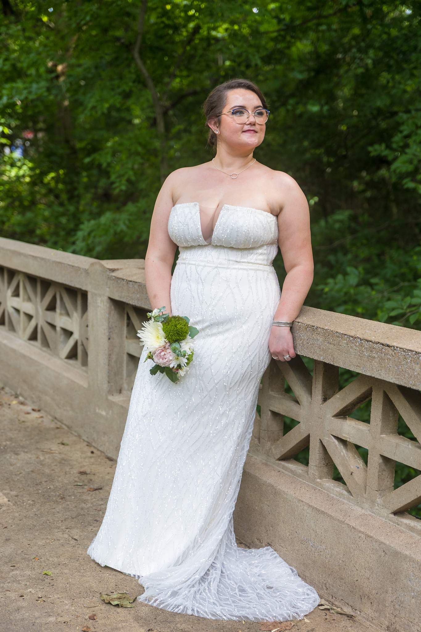 Bride leaning on a stone railing surrounded by trees at Emory