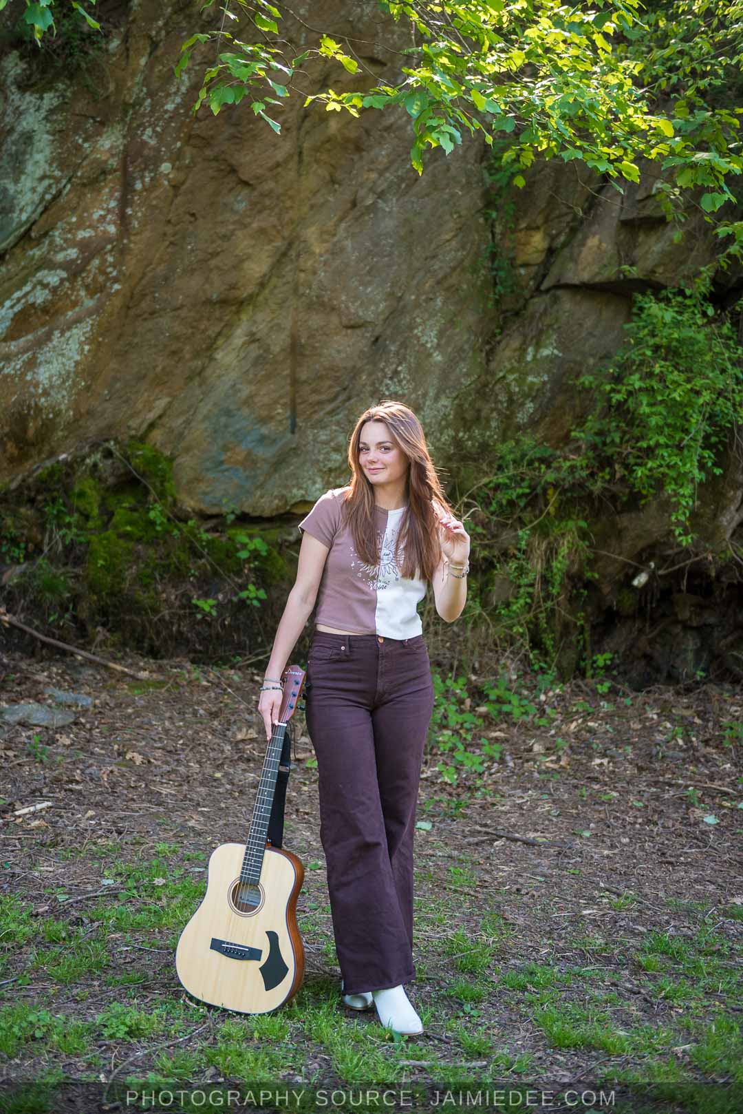 High school senior holding an acoustic guitar in front of a mossy rock outcrop at Olde Rope Mill Park in Woodstock, GA