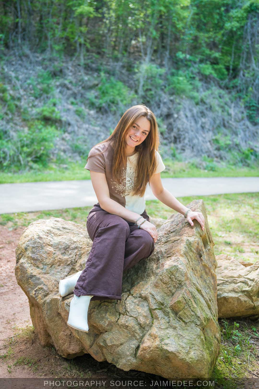 Senior sitting on a large boulder beside the paved walking path at Olde Rope Mill Park in Woodstock