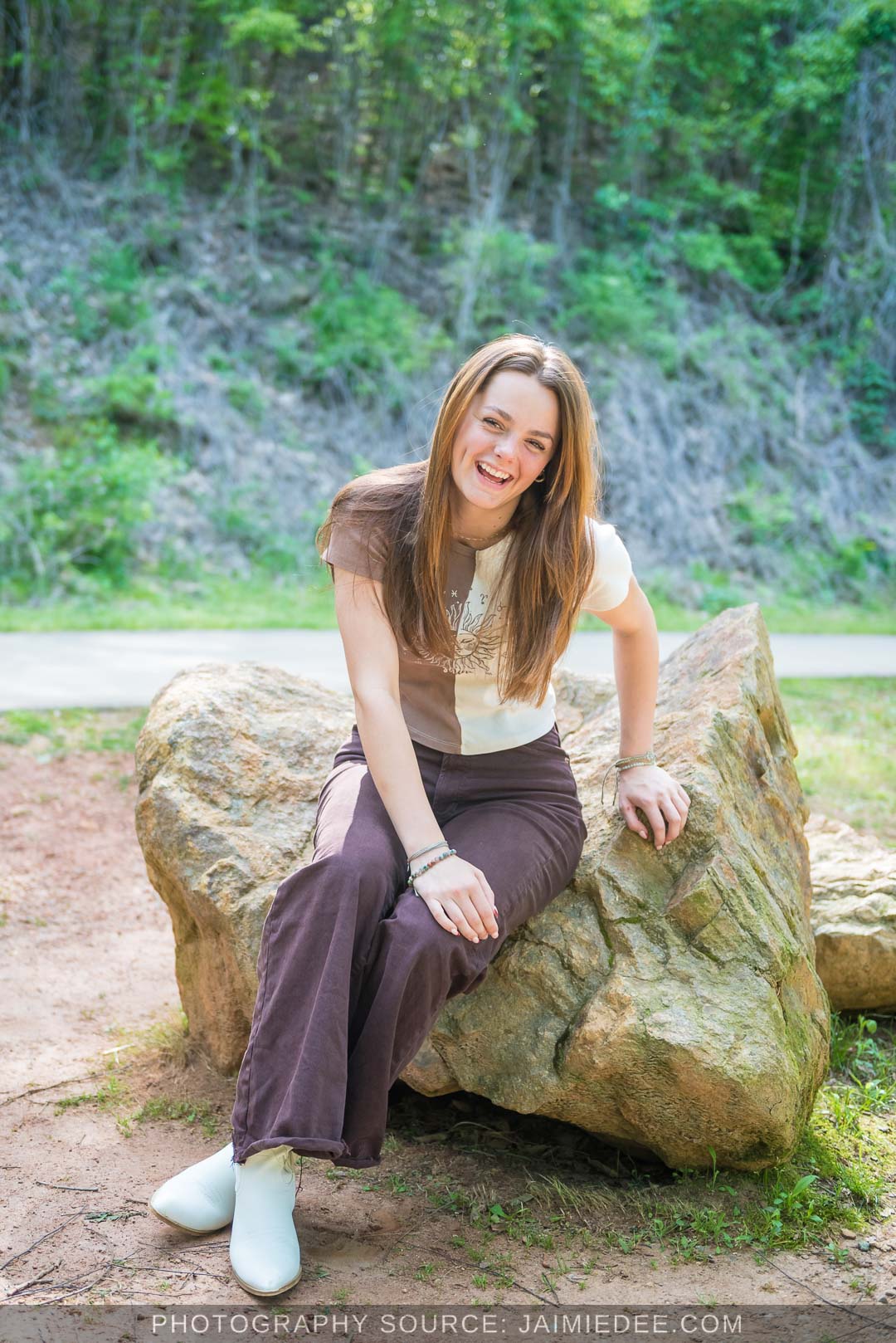 High school senior laughing while seated on a boulder near the walking path at Olde Rope Mill Park