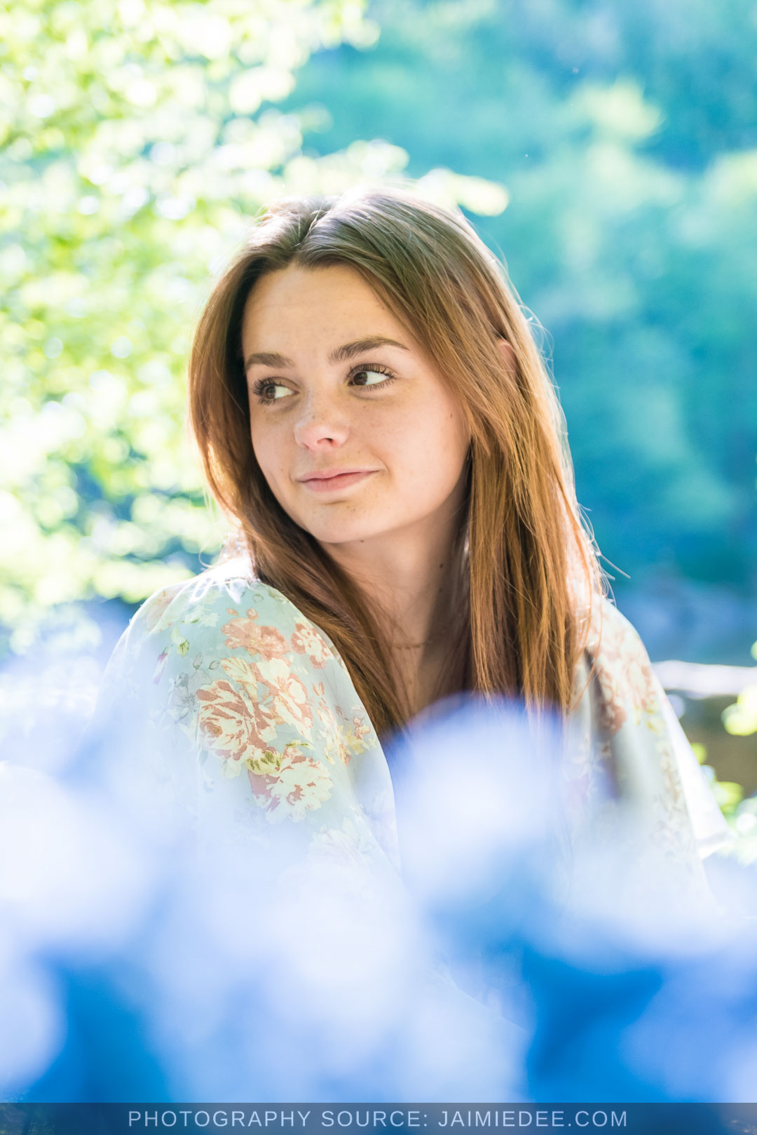 Close-up senior portrait with blue flowers in the foreground and the Little River behind her at Olde Rope Mill Park