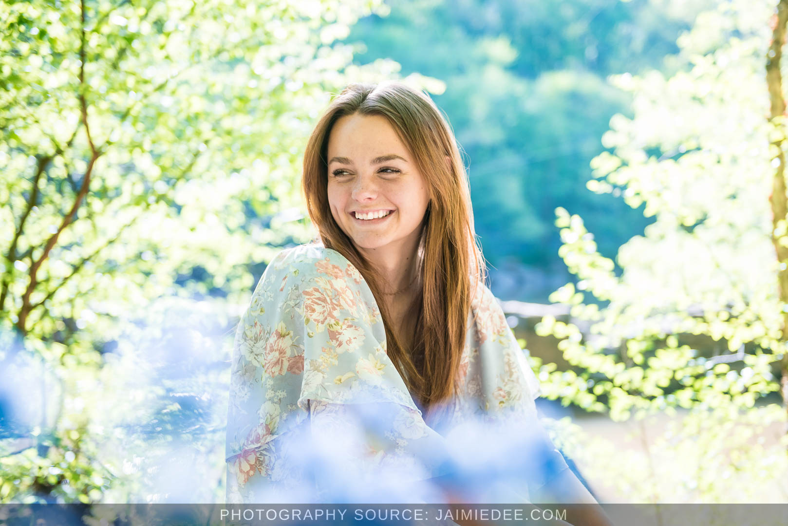 Senior in a floral dress smiling by the Little River at Olde Rope Mill Park, framed by spring leaves