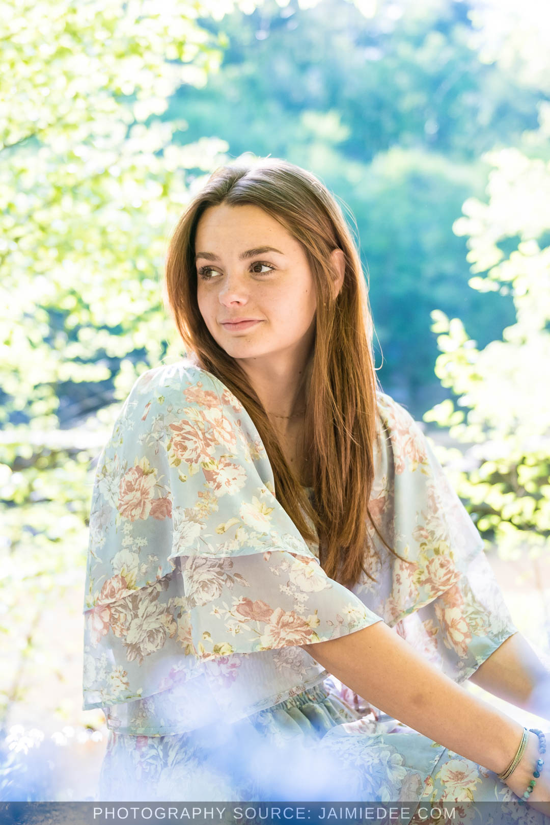 High school senior in a floral dress looking away from the camera beside the river at Olde Rope Mill Park