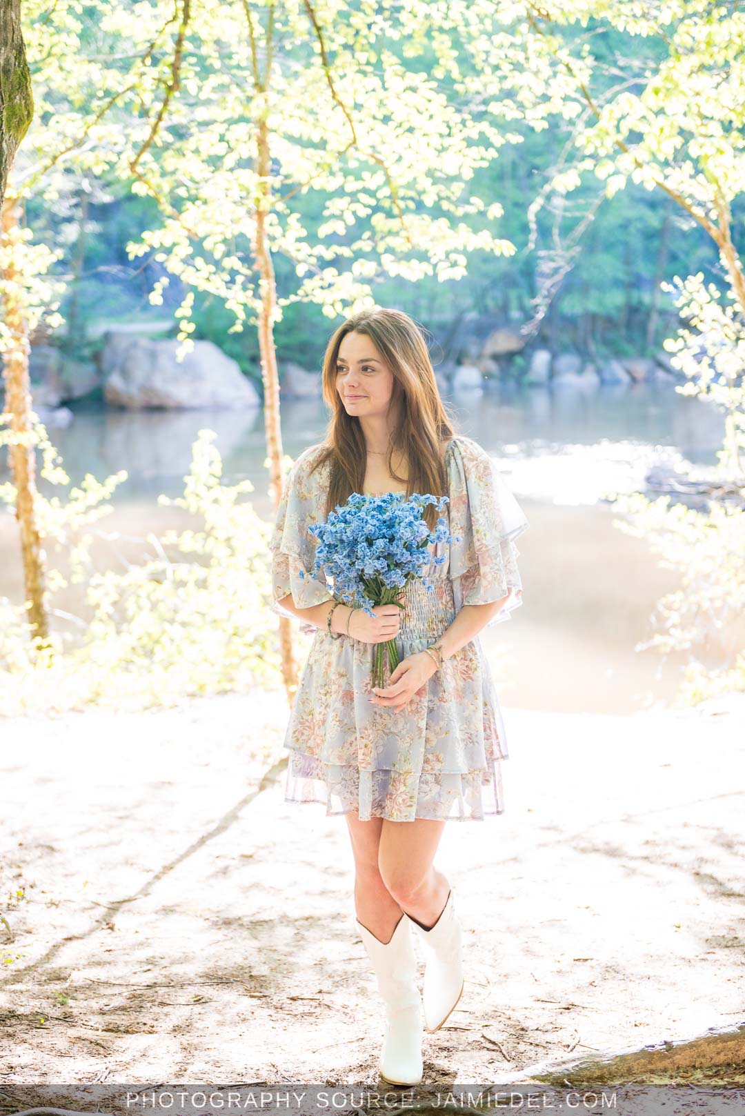 Full-length senior portrait in a floral dress and white boots on the Little River shoreline at Olde Rope Mill Park