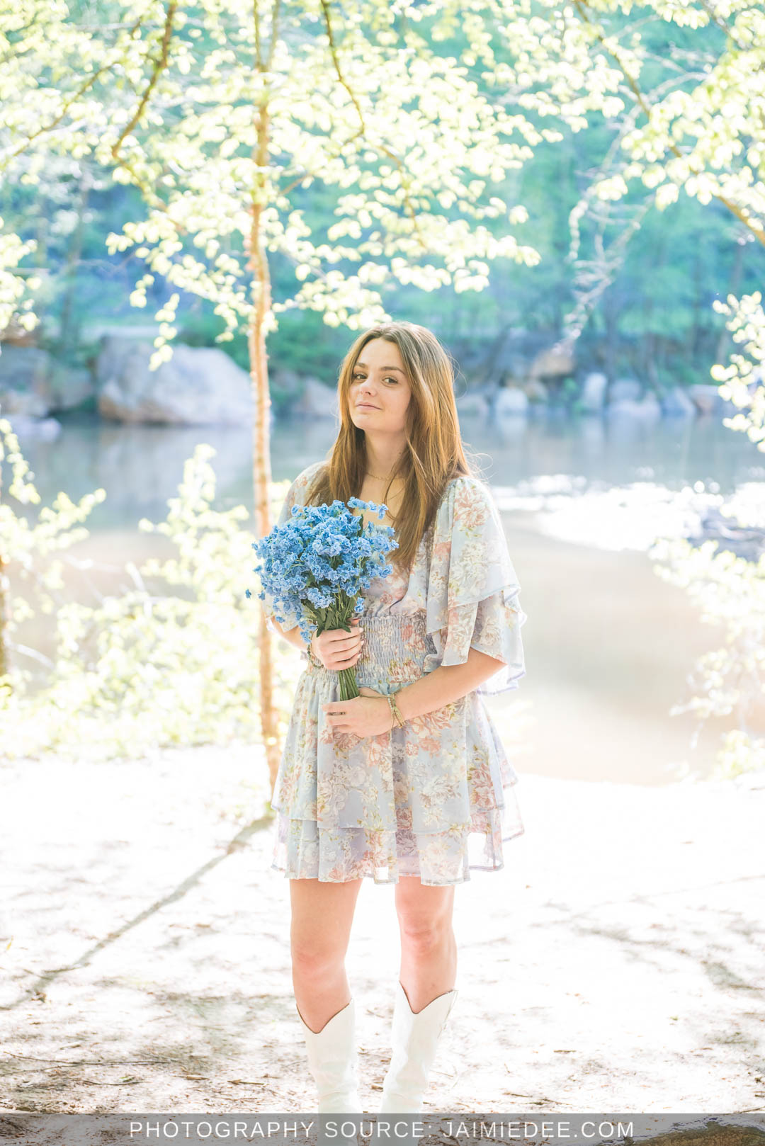 High school senior holding a bouquet of blue flowers among trees by the river at Olde Rope Mill Park