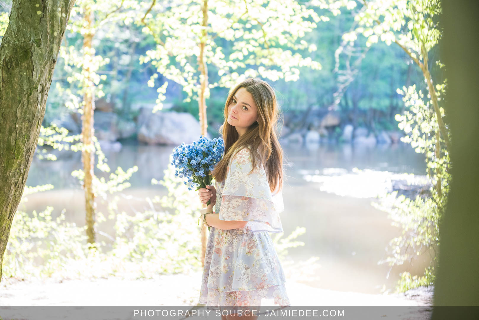 Senior portrait framed by tree trunks with the Little River in the background at Olde Rope Mill Park in Woodstock