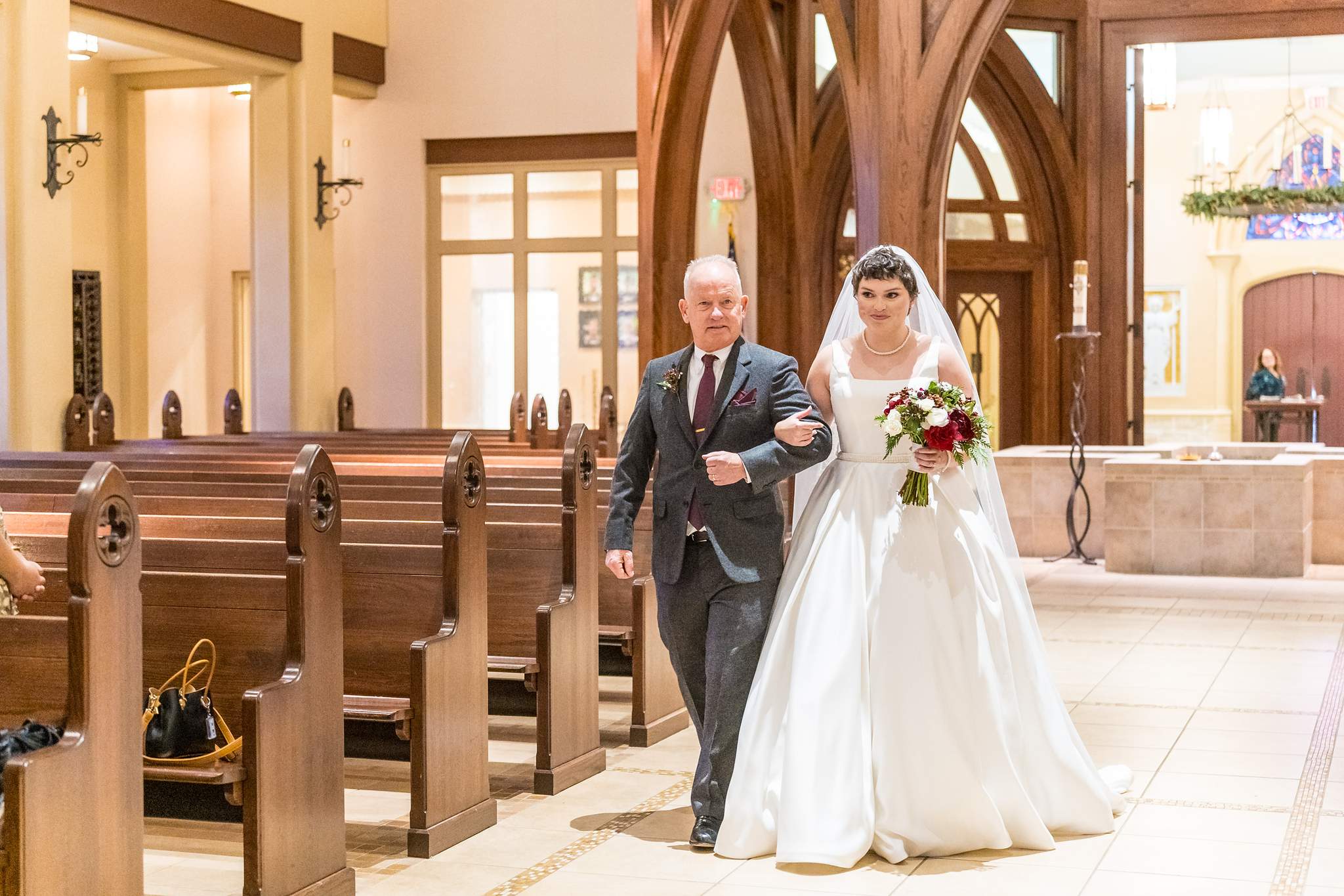 Bride walking down the aisle with her escort at Our Lady of the Assumption Catholic Church