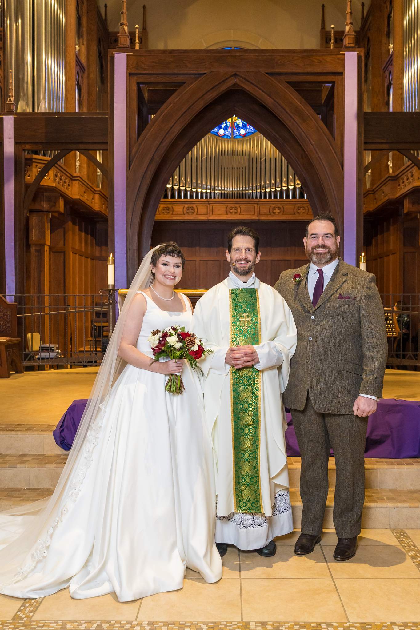 Couple with the priest at the altar after their wedding at Our Lady of the Assumption