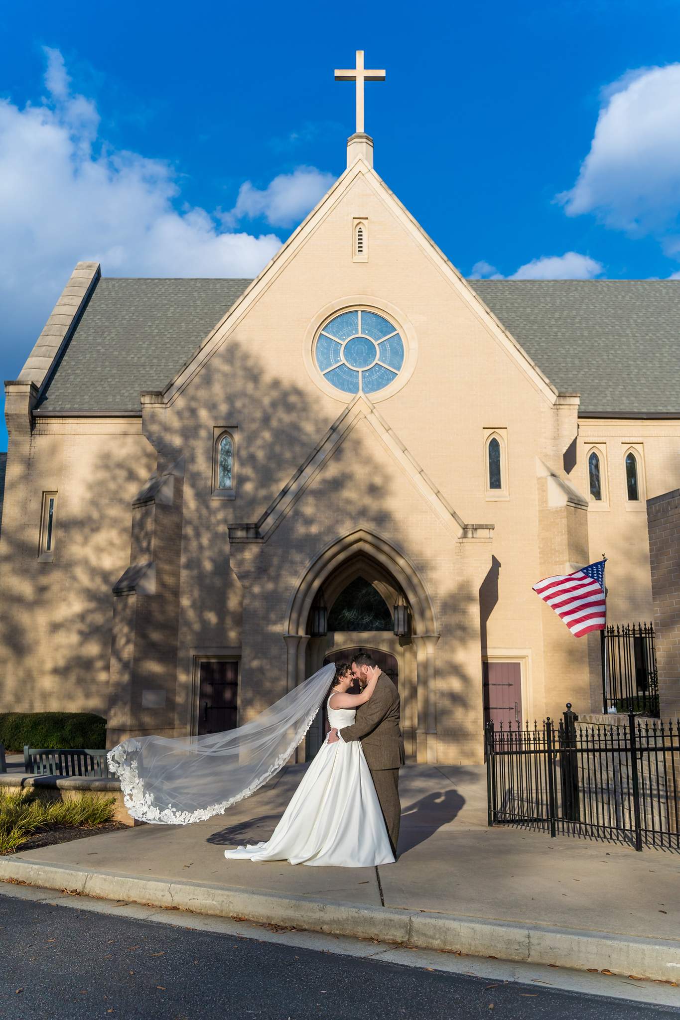 Couple kissing with the veil blowing outside Our Lady of the Assumption Catholic Church