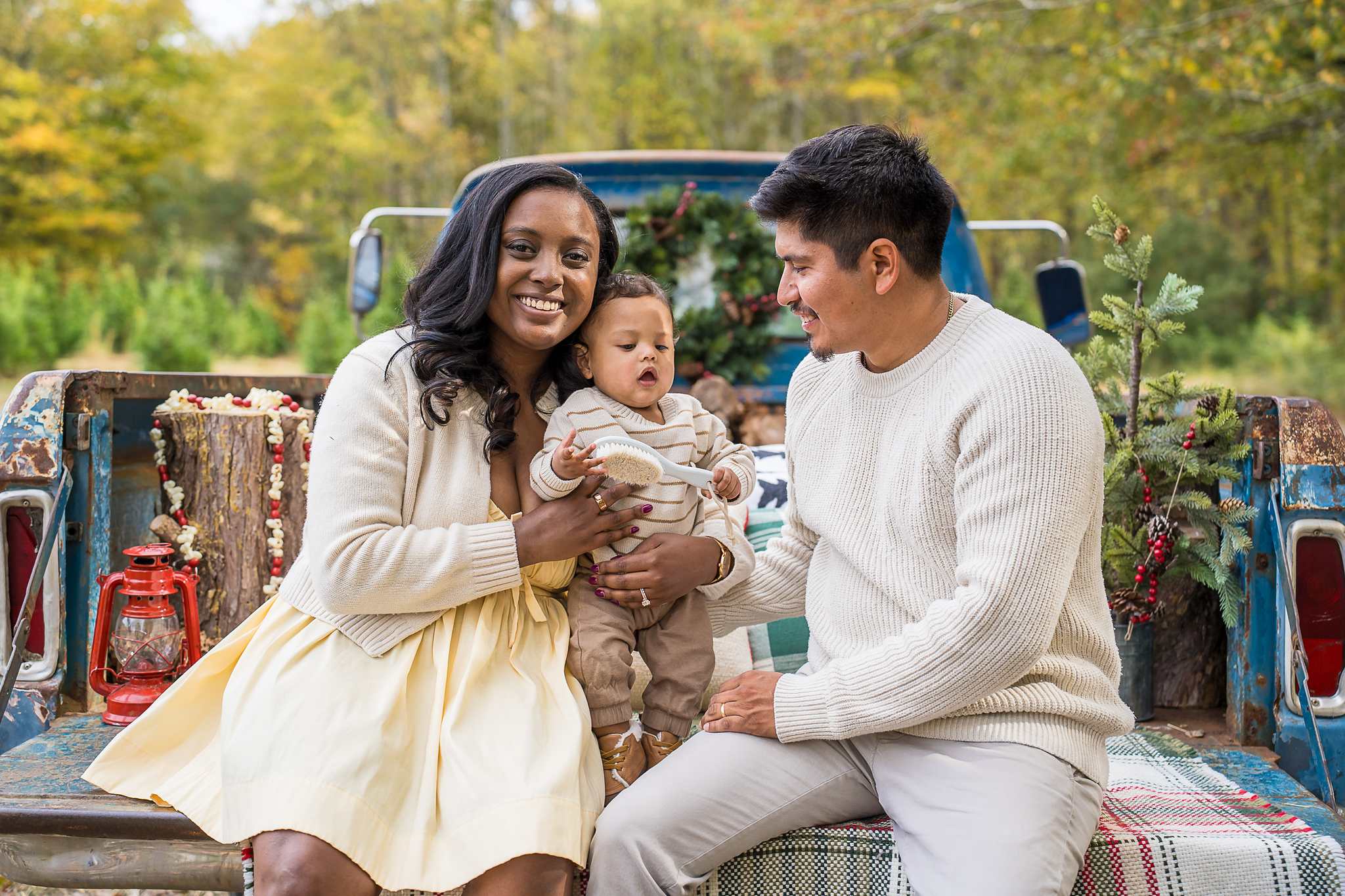 Parents and baby sitting on the plaid-draped tailgate of the 1965 Blue Christmas Truck