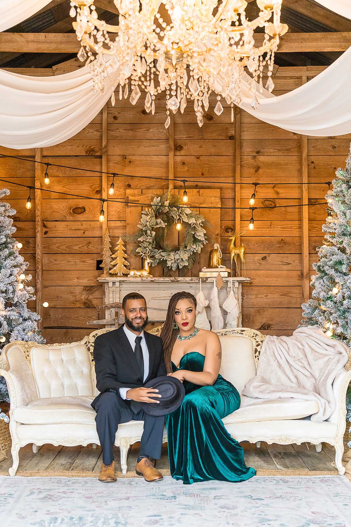 Couple in an emerald velvet gown and dark suit on the white settee in the Christmas Barn at Prospect Farms