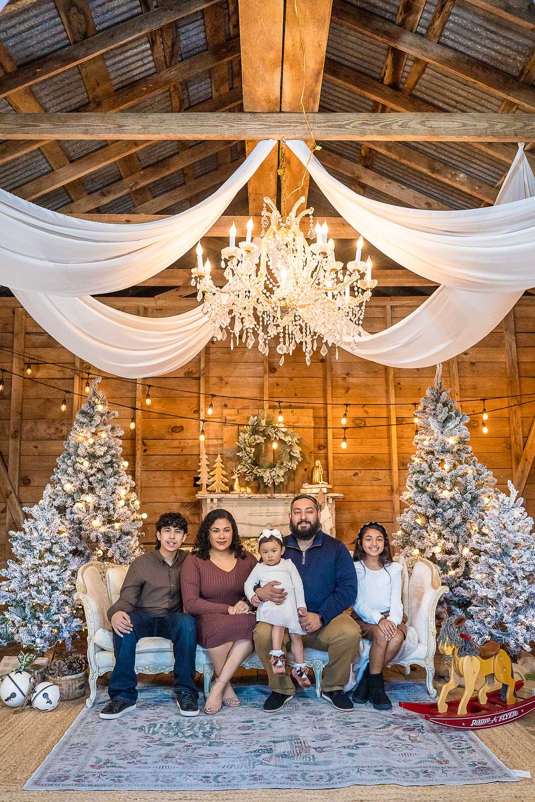 Family of six on the white settee in the Christmas Barn set at Prospect Farms under a crystal chandelier