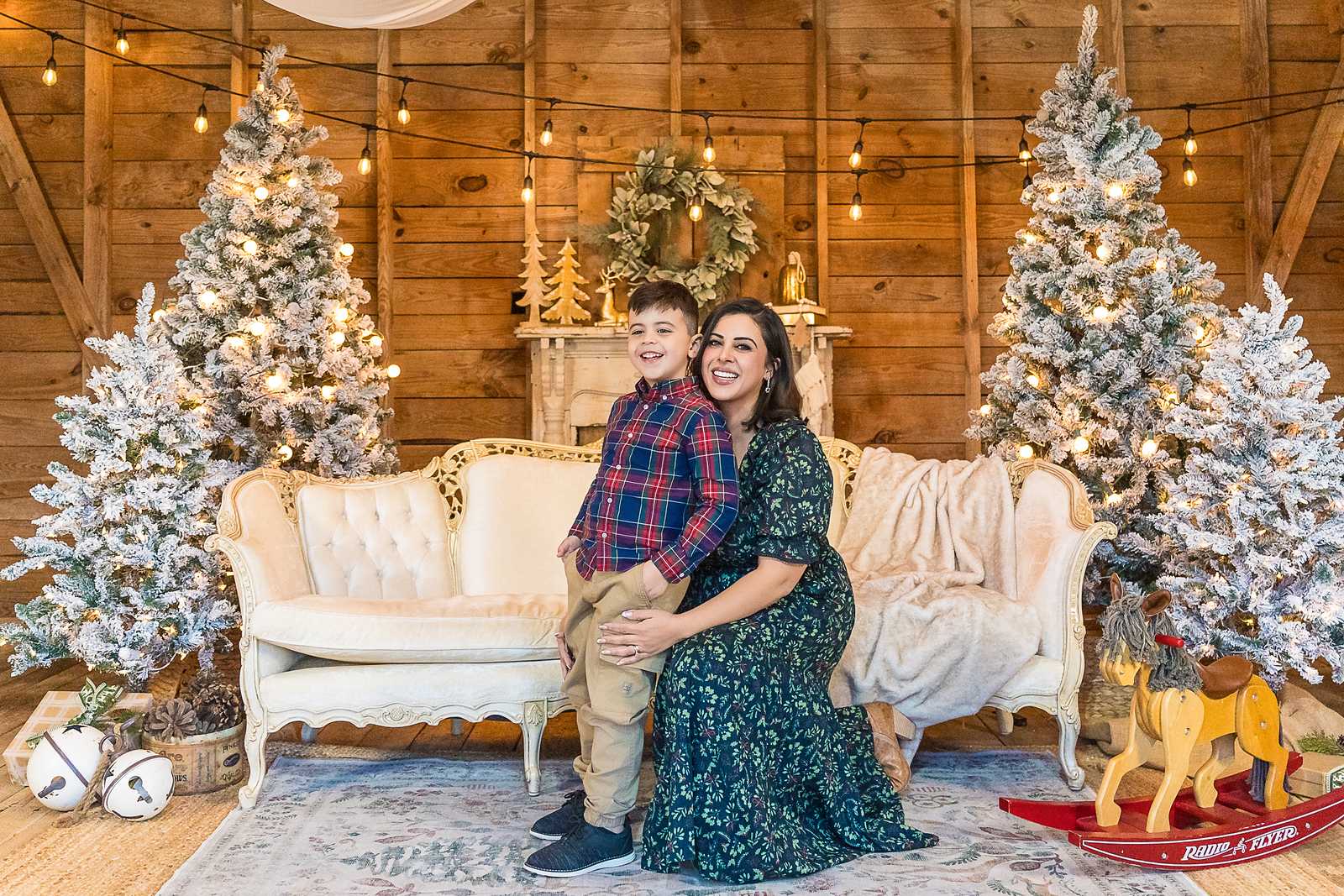 Mother and son on the white settee beside flocked trees in the Christmas Barn at Prospect Farms