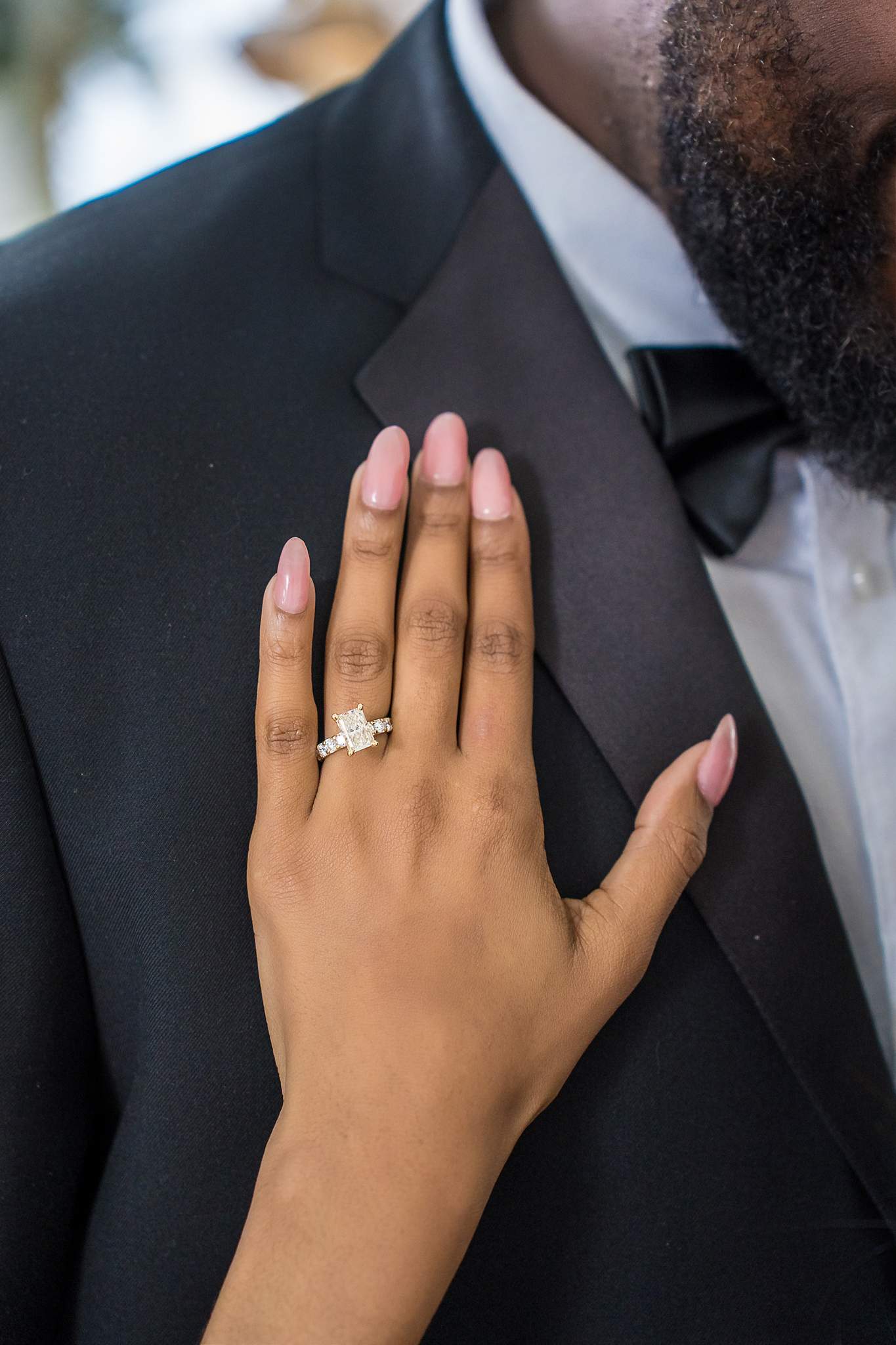 Close-up of an engagement ring on a hand resting on a tuxedo lapel