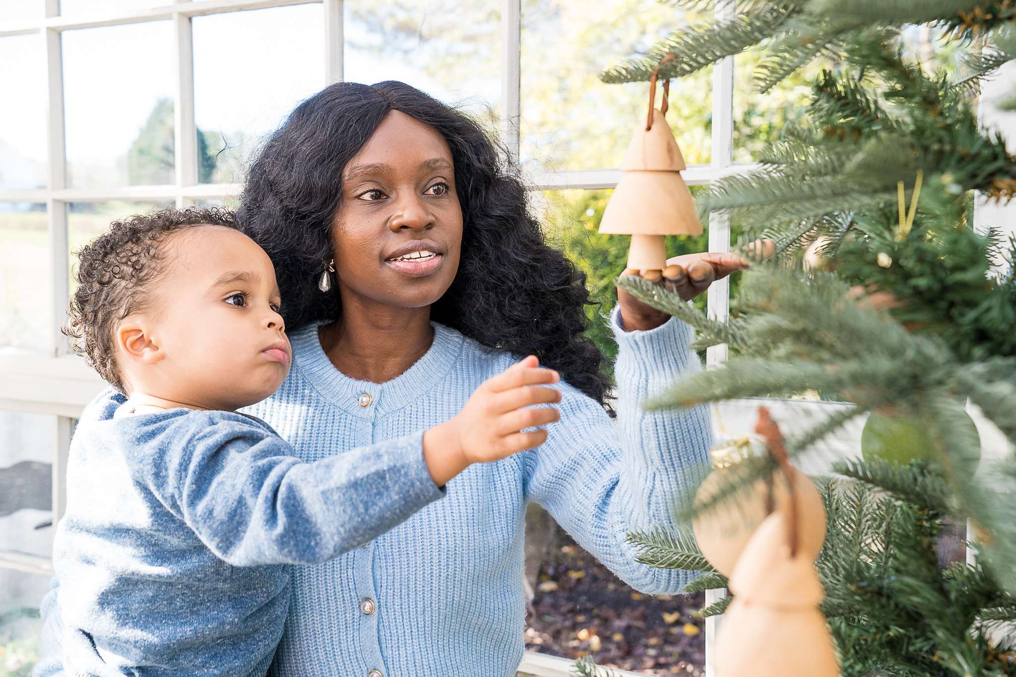 Mother and toddler reaching for ornaments on a Christmas tree in the Greenhouse at Prospect Farms