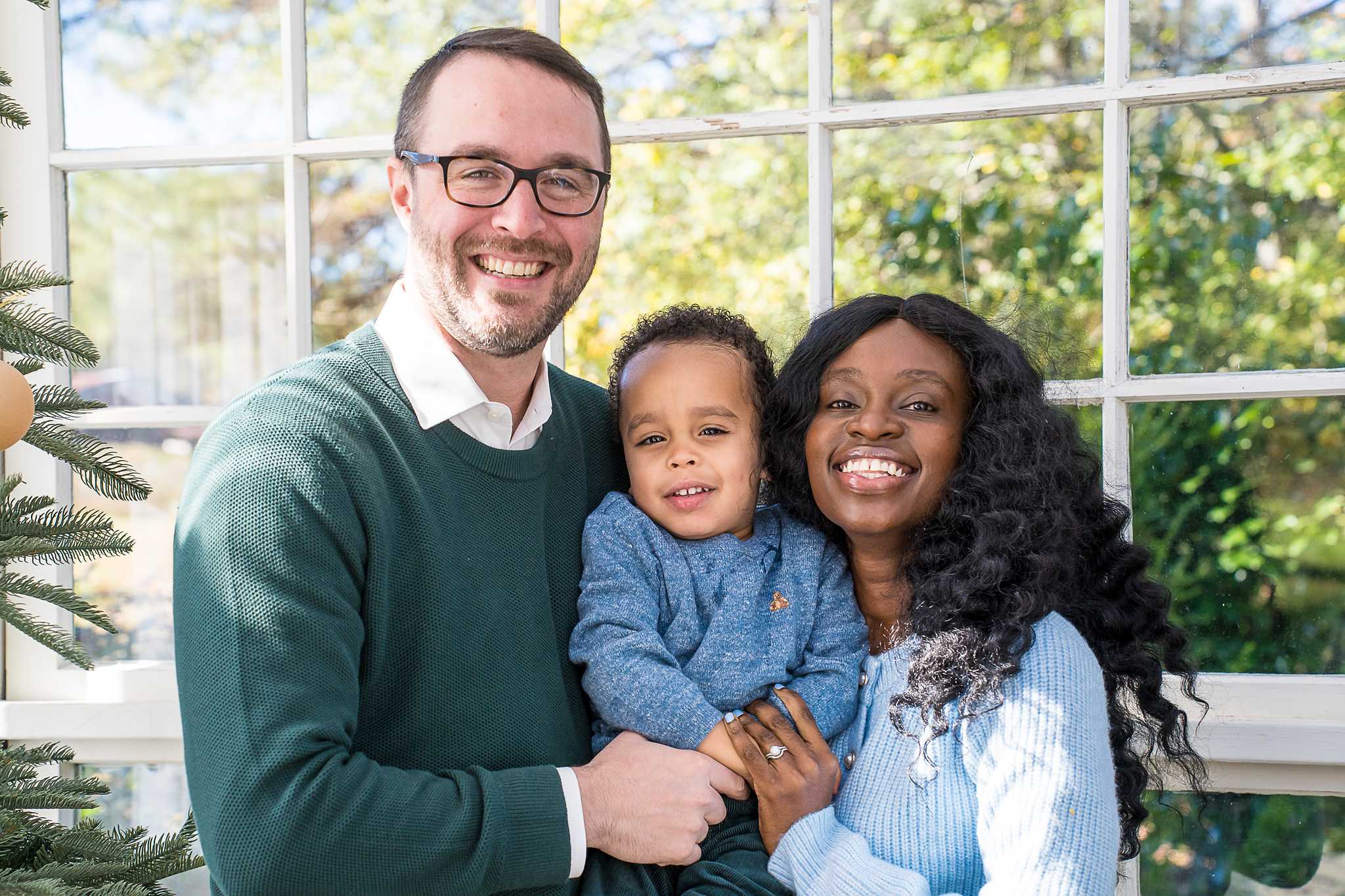 Parents holding their toddler beside a Christmas tree in the Greenhouse at Prospect Farms