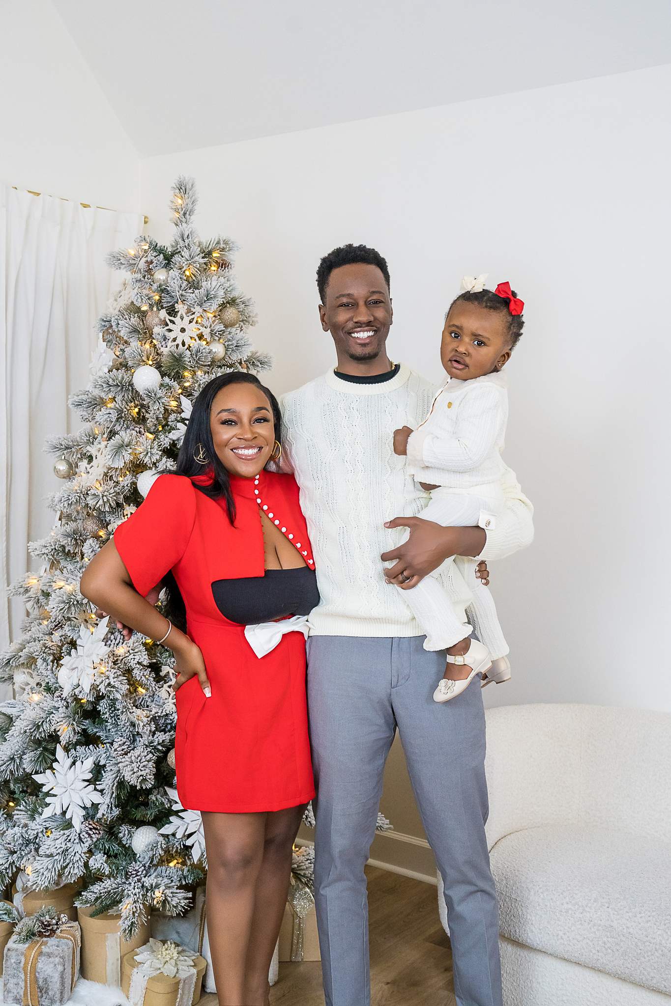 Family in red, white and gray beside a flocked Christmas tree in the Lounge Christmas set
