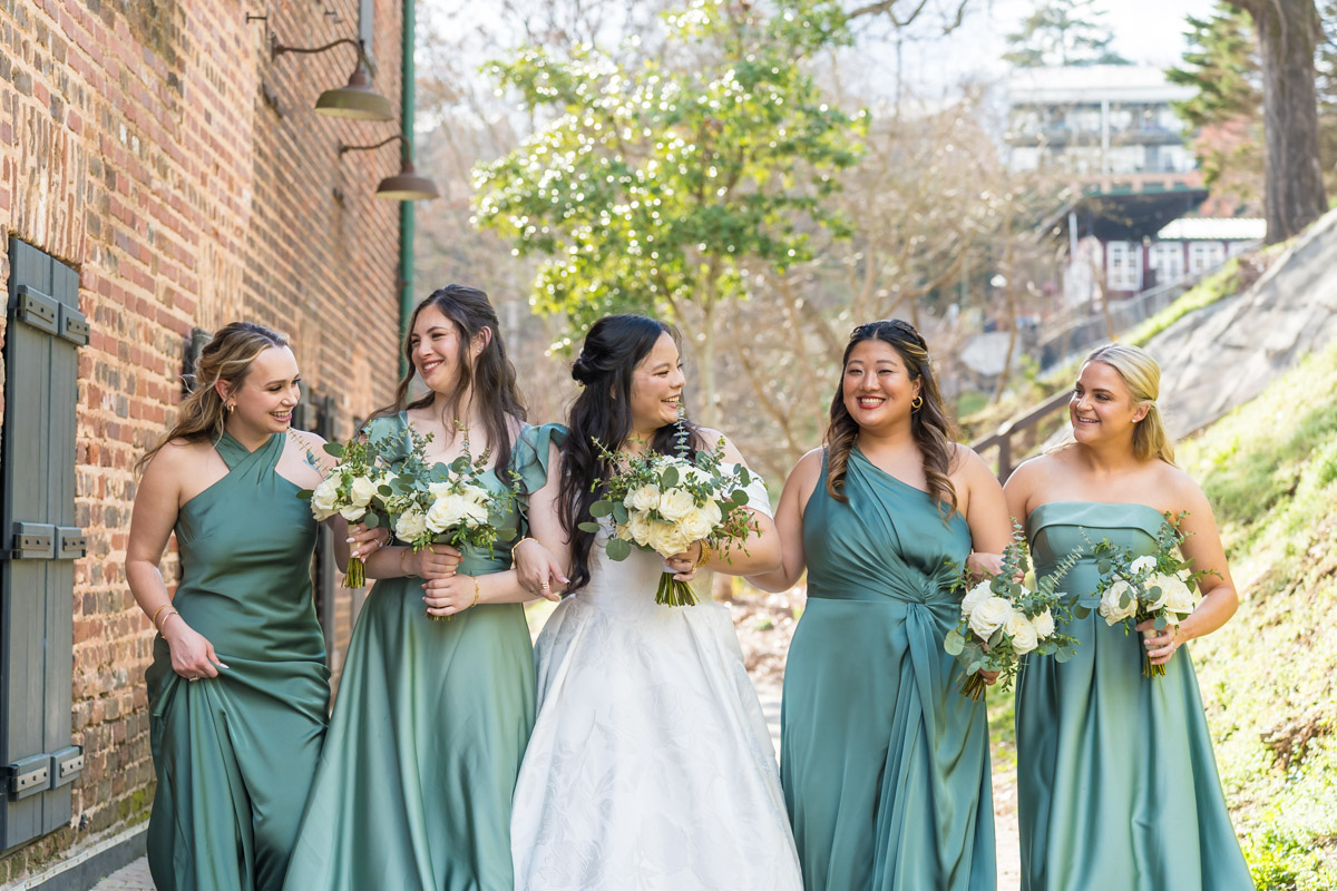 Bride and bridesmaids by brick wall at park next to Roswell Mill Club wedding
