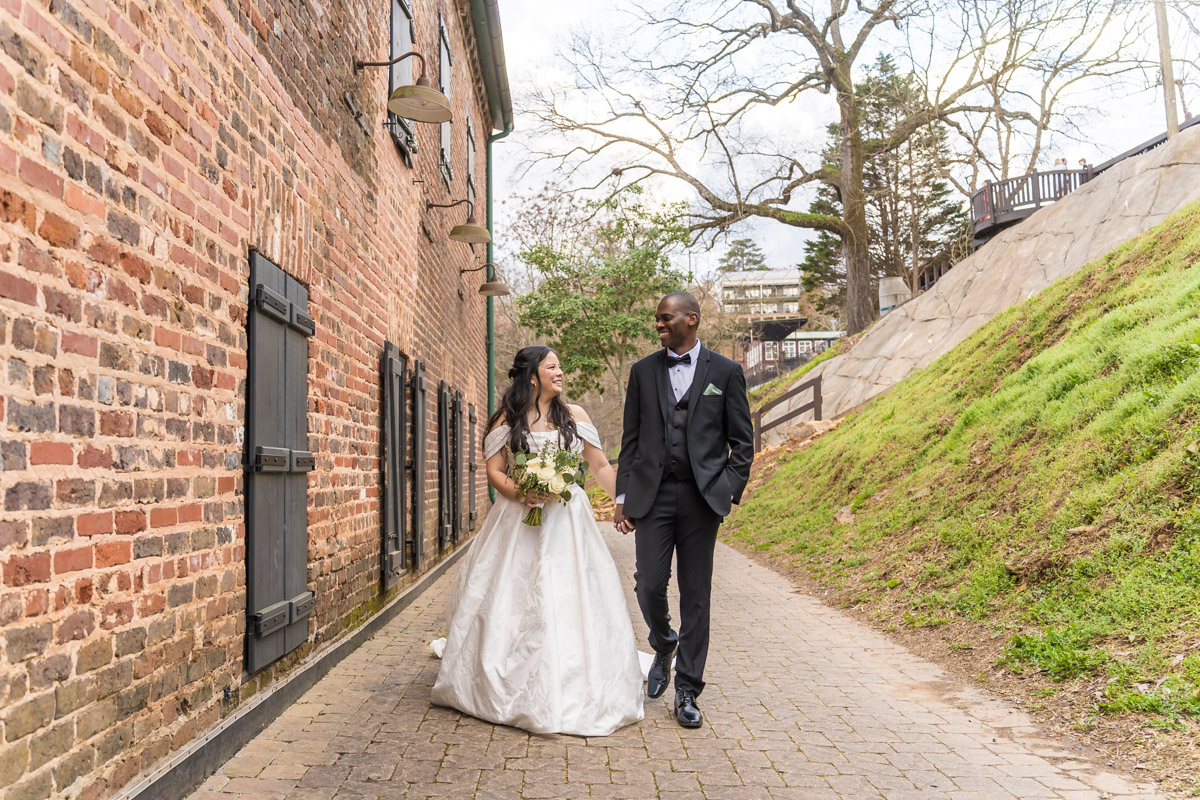 Bride and groom walking by brick building in downtown Roswell park for Roswell Mill Club wedding photos