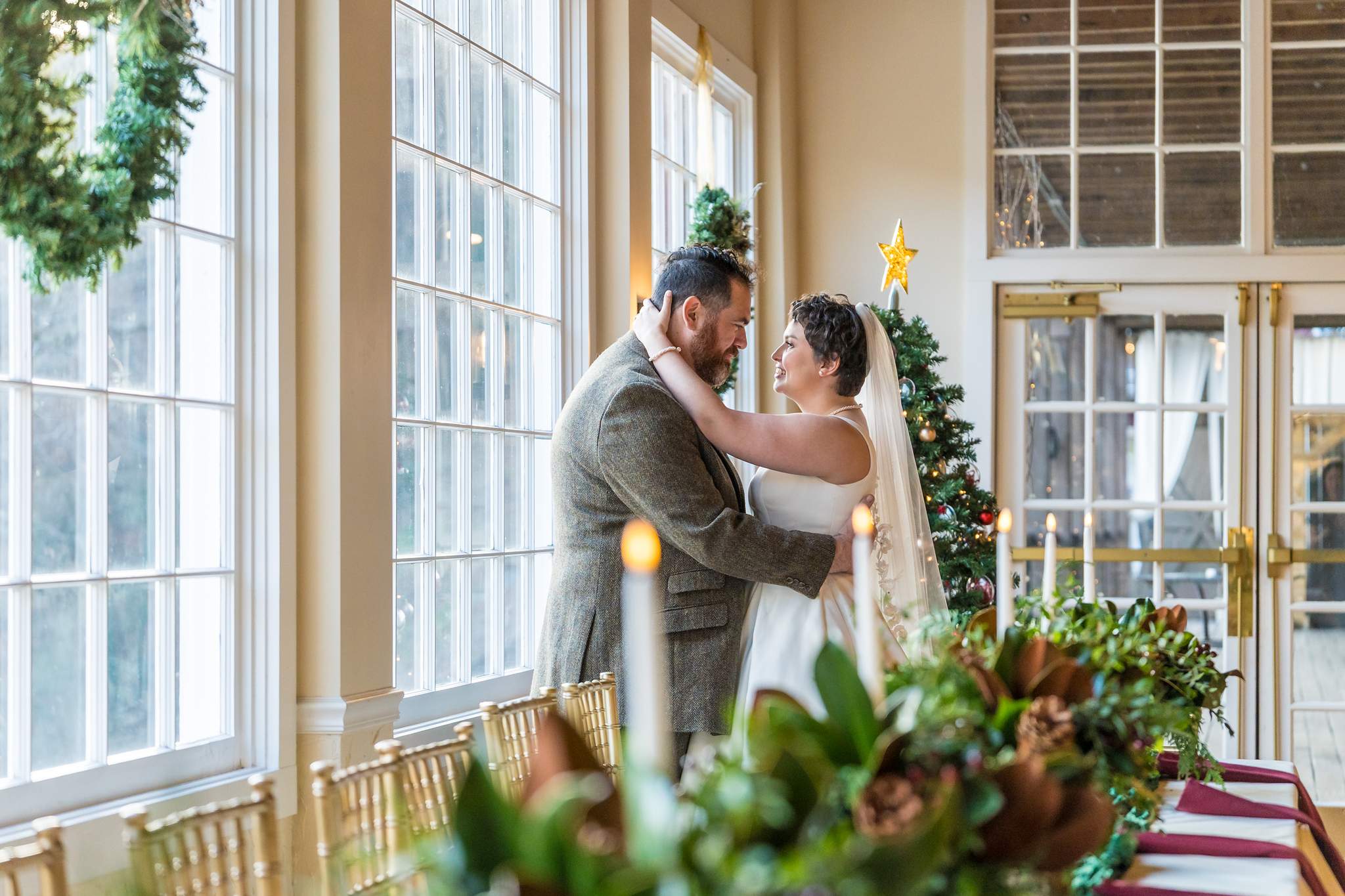 Couple embracing by the tall windows at a Roswell Mill Club Christmas wedding