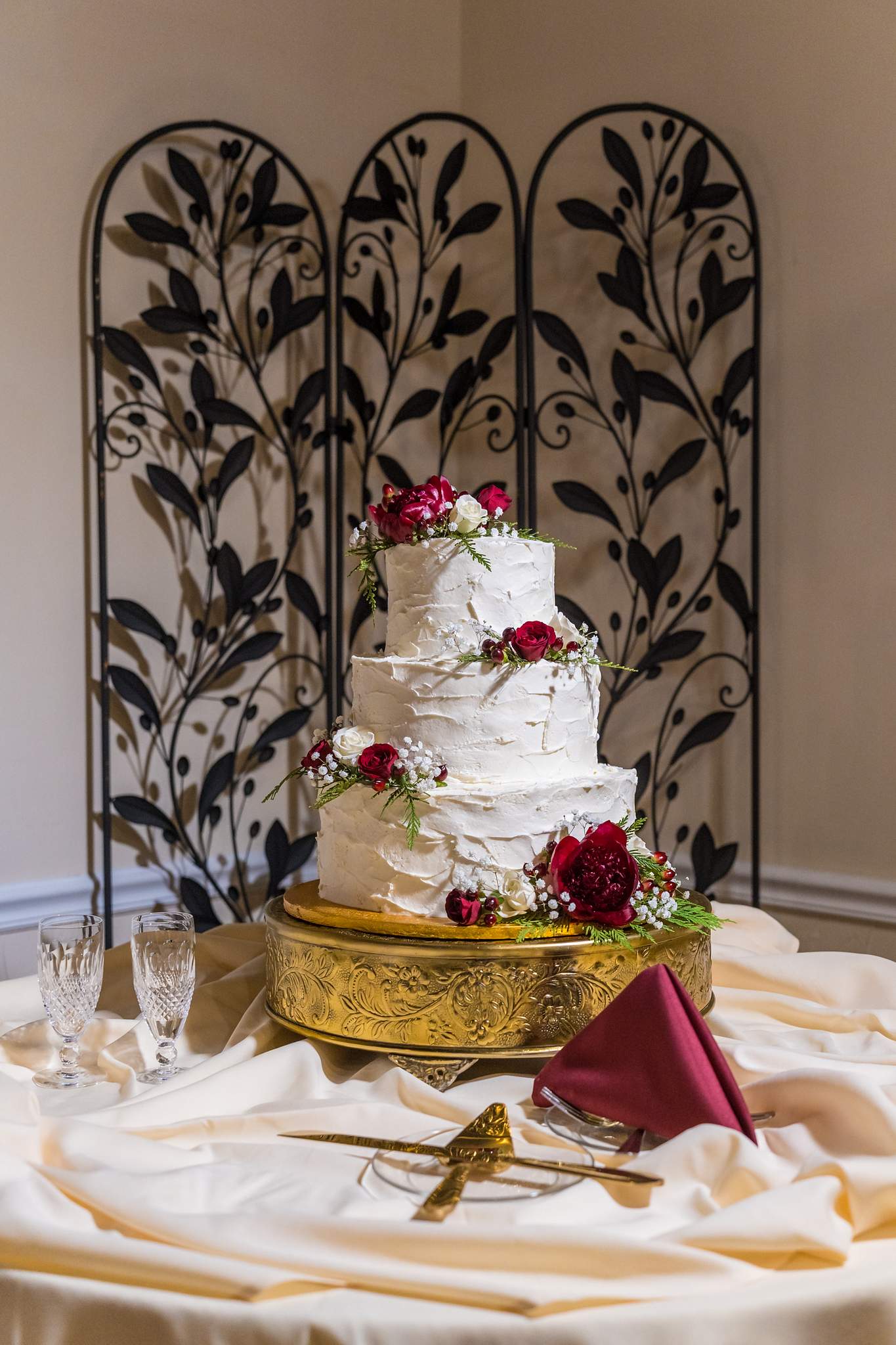 Wedding cake with red flowers in front of a decorative screen at Roswell Mill Club
