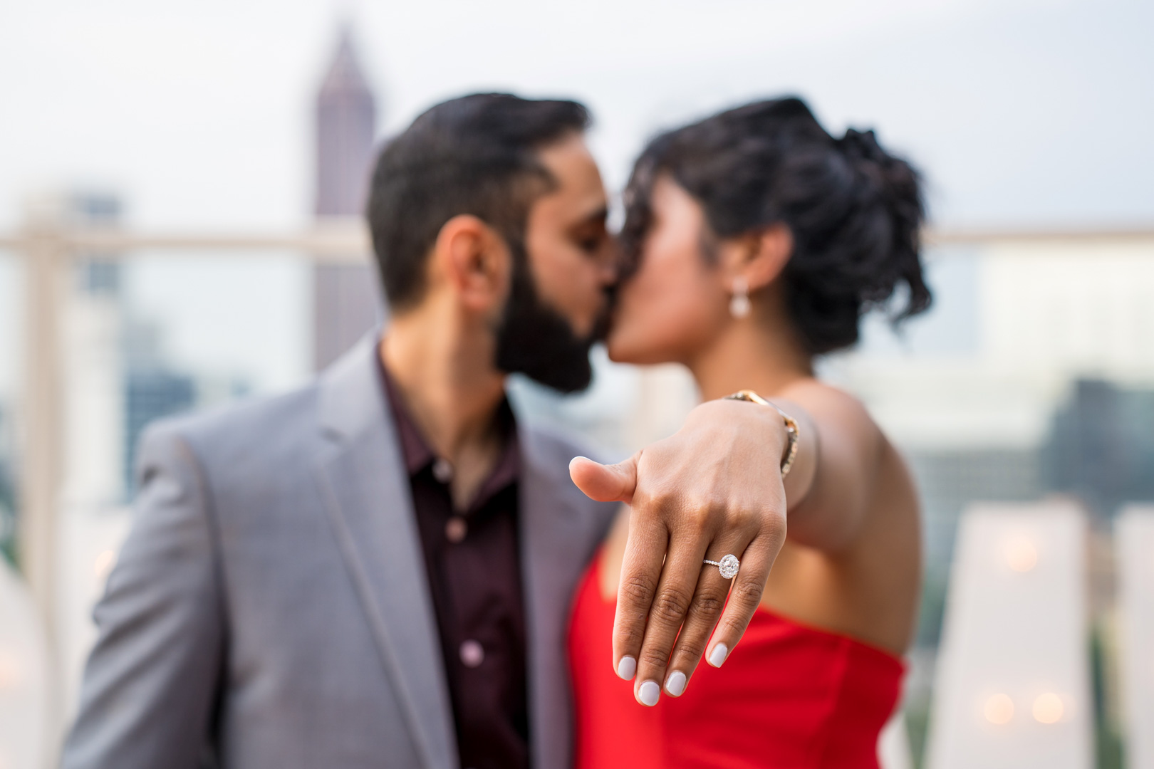 Newly engaged couple kissing as she holds out her hand to show her engagement ring