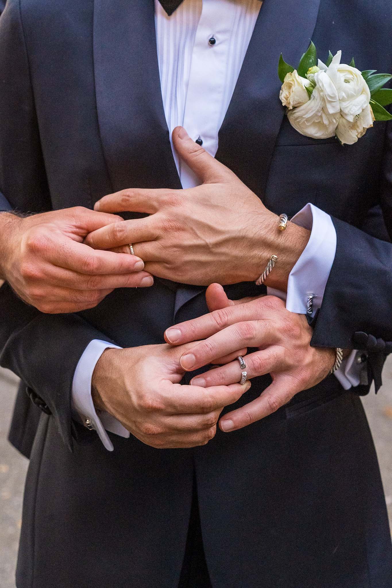 Close up of hands and wedding rings with a white boutonniere