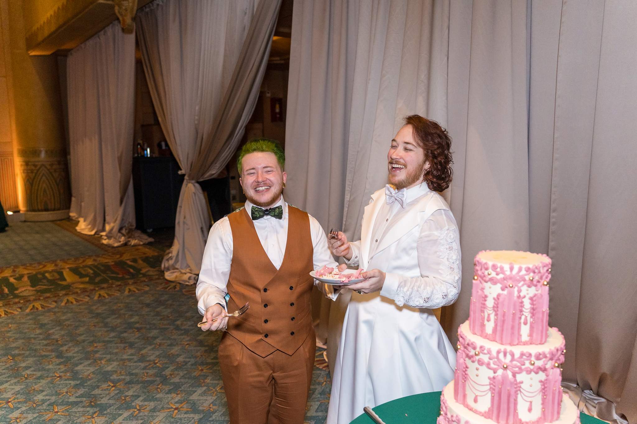 Couple laughing beside their wedding cake in the Egyptian Ballroom