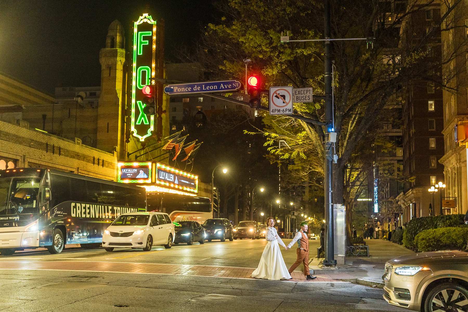 Couple holding hands as they cross the street at night in front of the glowing Fox Theatre sign in Midtown Atlanta