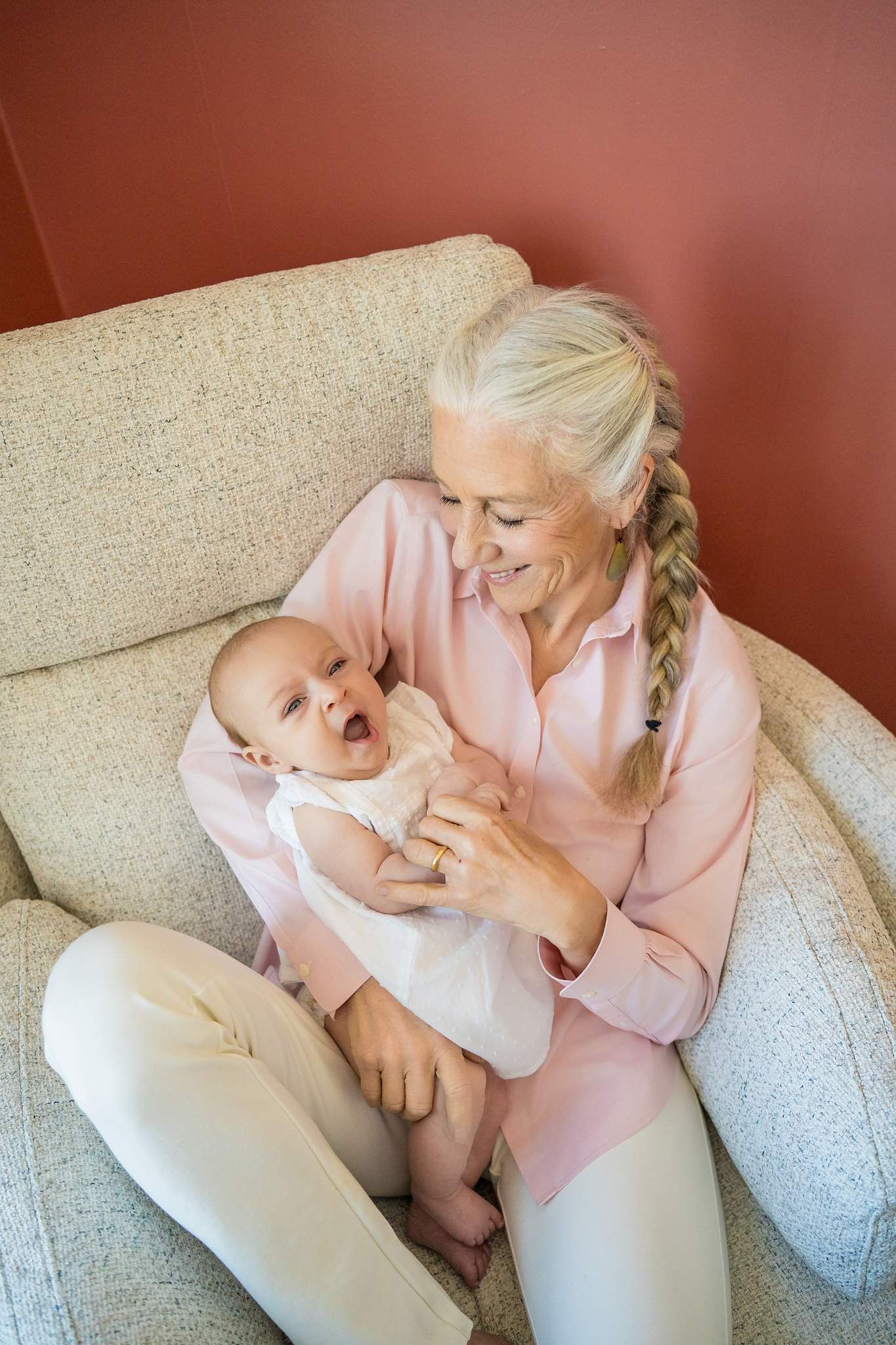 Family member in a blush pink shirt and cream pants cradling the baby on a boucle armchair