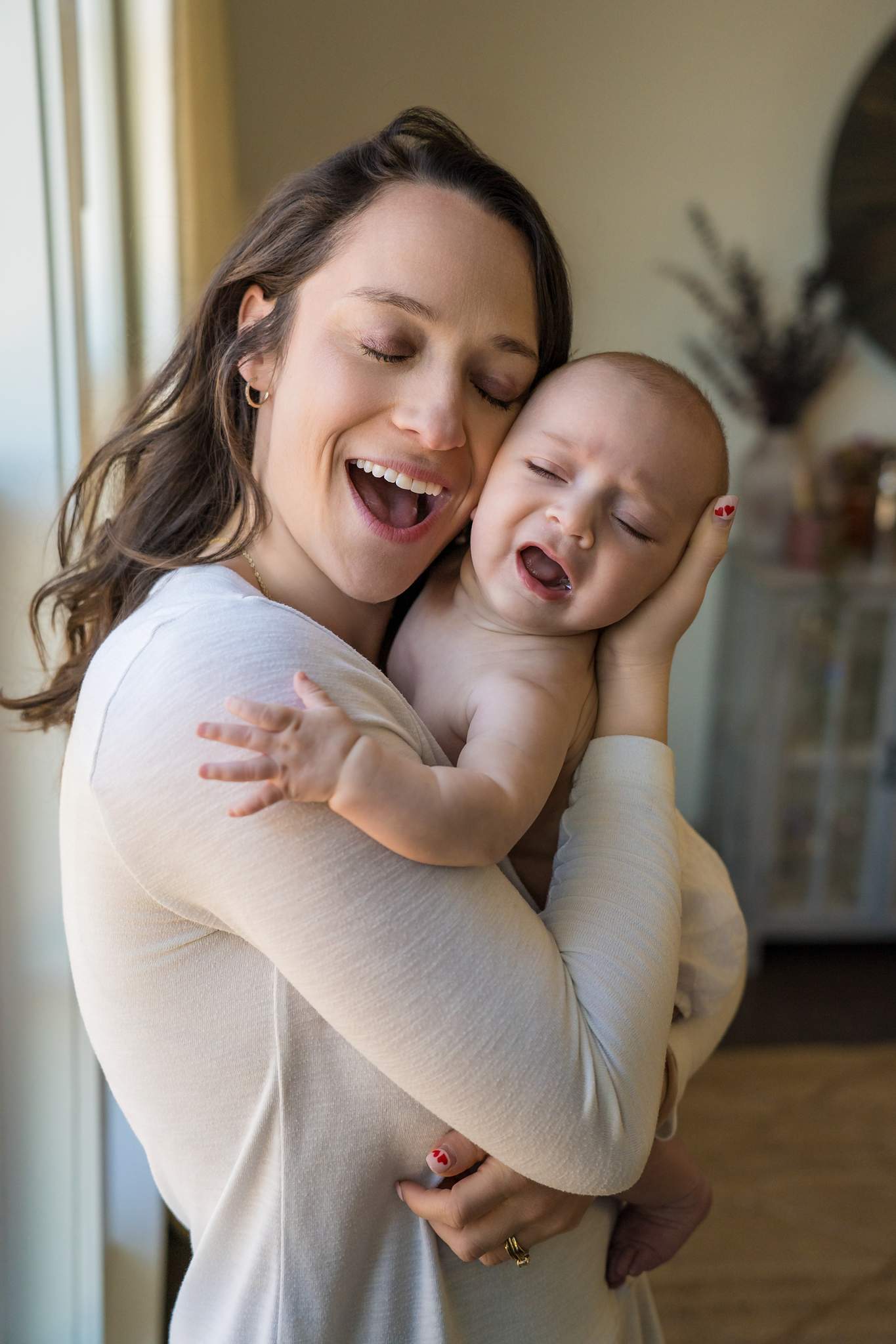 Mom in a soft cream knit top cuddling her fussy baby cheek to cheek at home