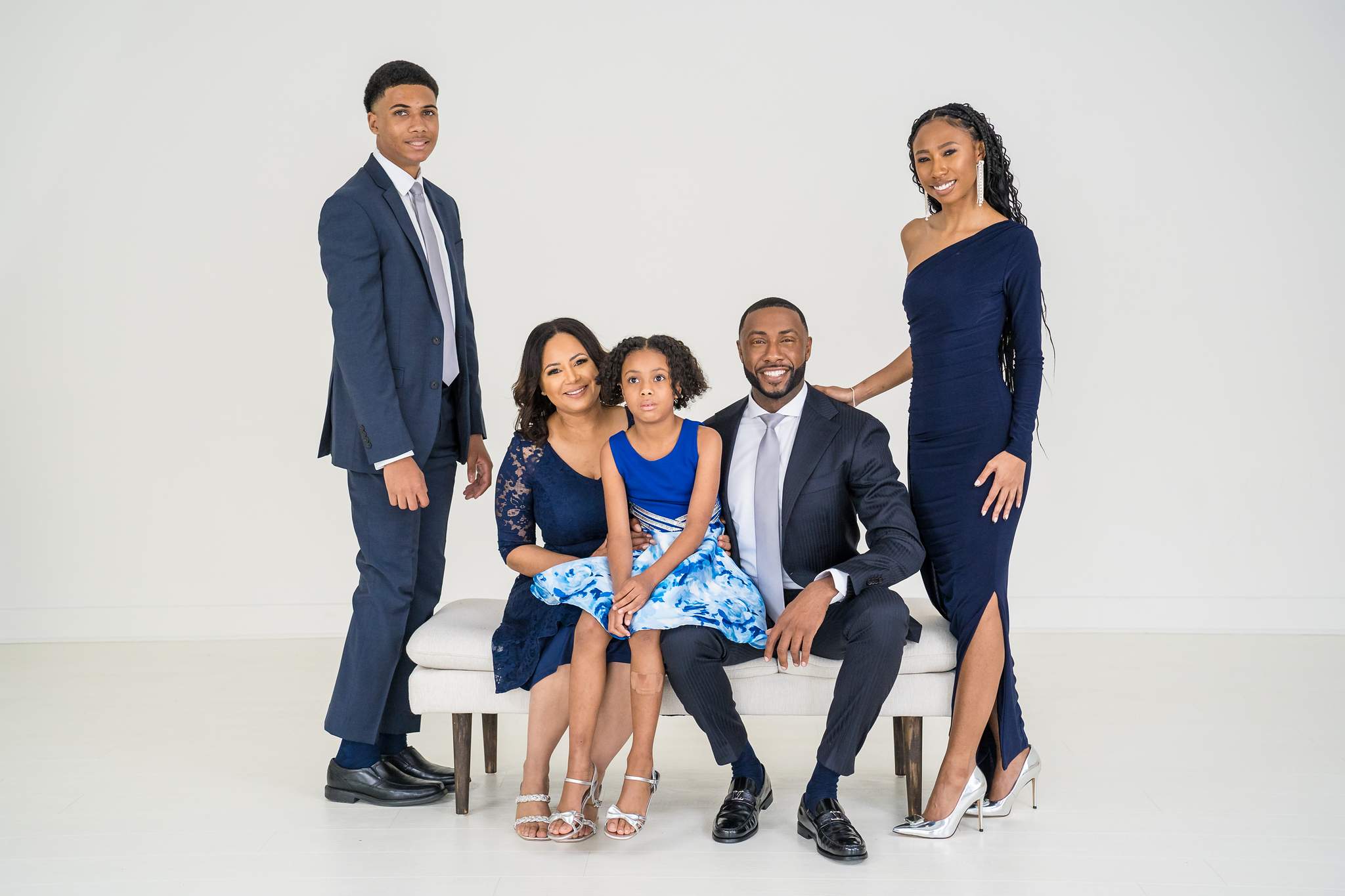 Family on a white bench in navy suits, navy dresses and royal blue florals in a white studio