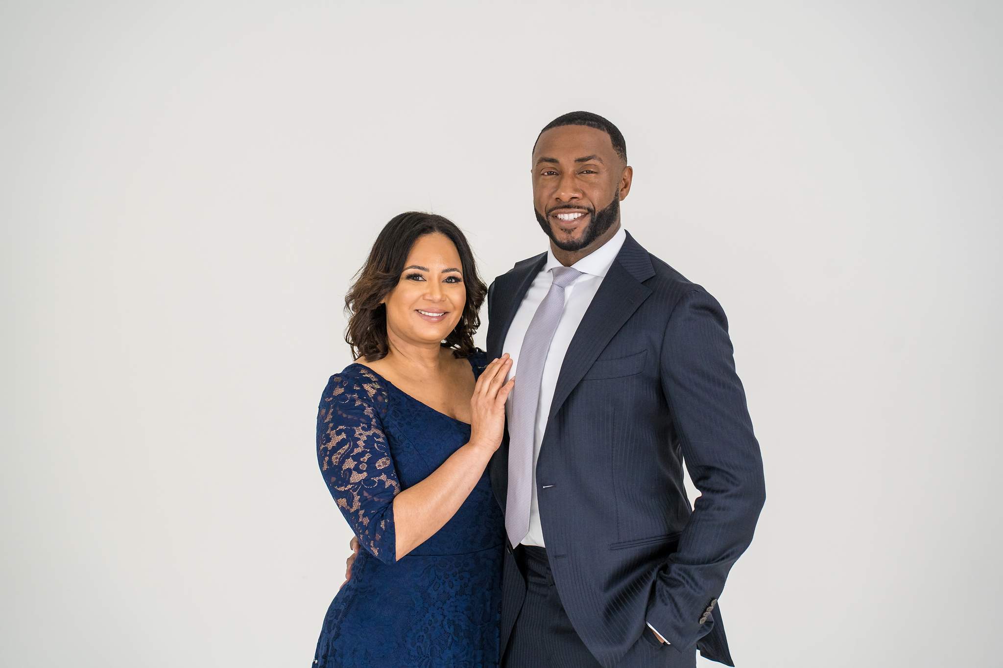 Couple in a navy suit with silver tie and navy lace dress on a white studio set