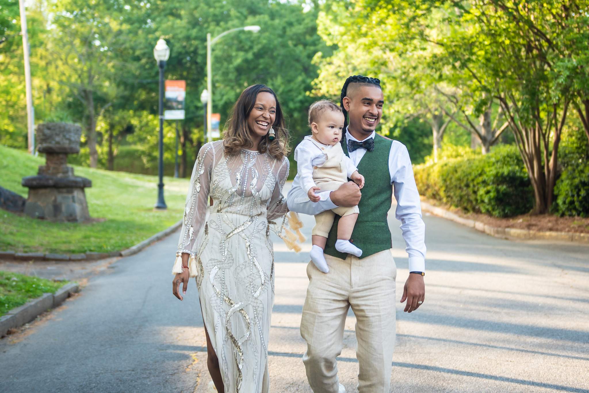 Cream beaded gown, linen trousers and an olive vest as parents walk their baby along a park road