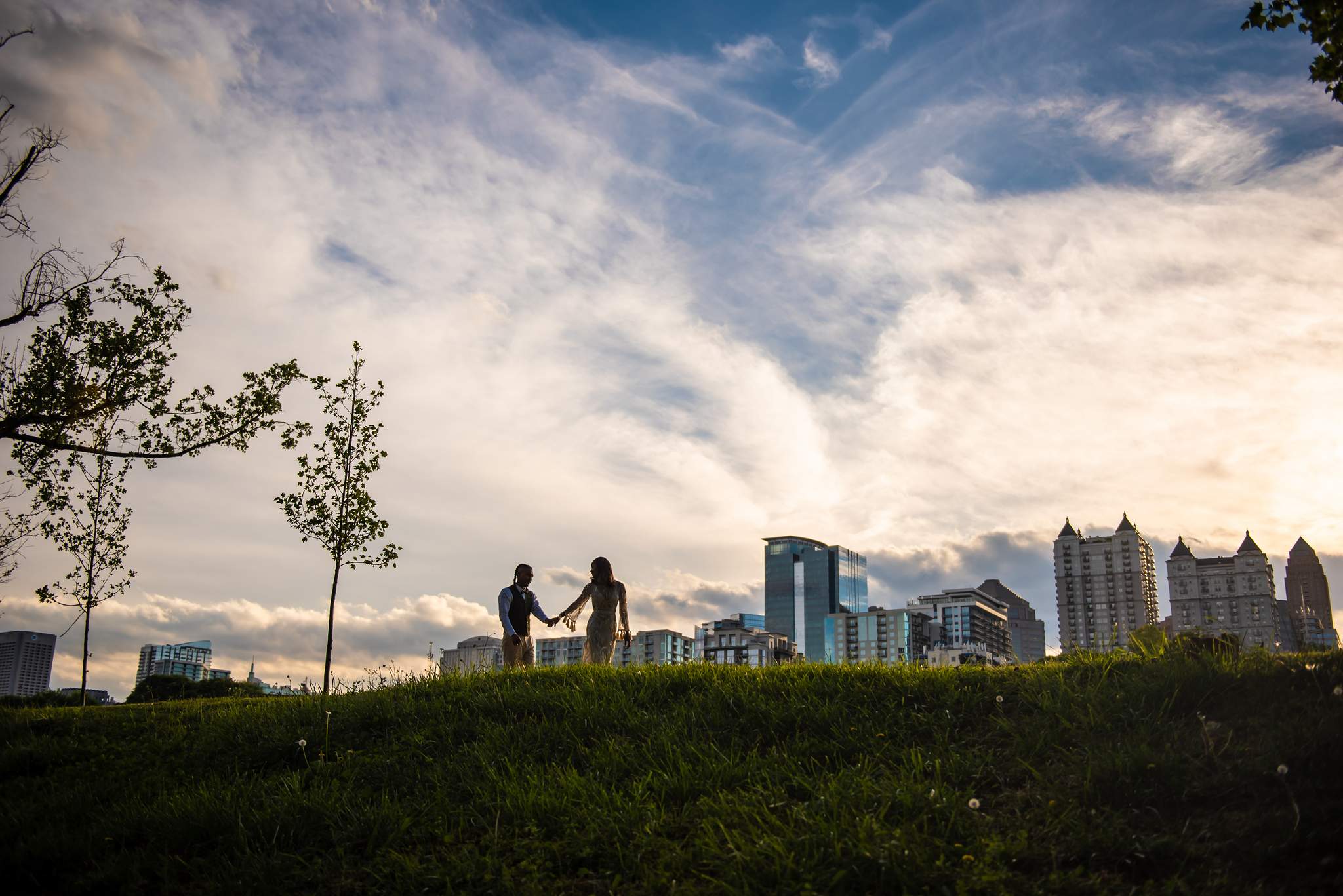 Parents silhouetted holding hands on a grassy hill against a sunset sky and the Atlanta skyline