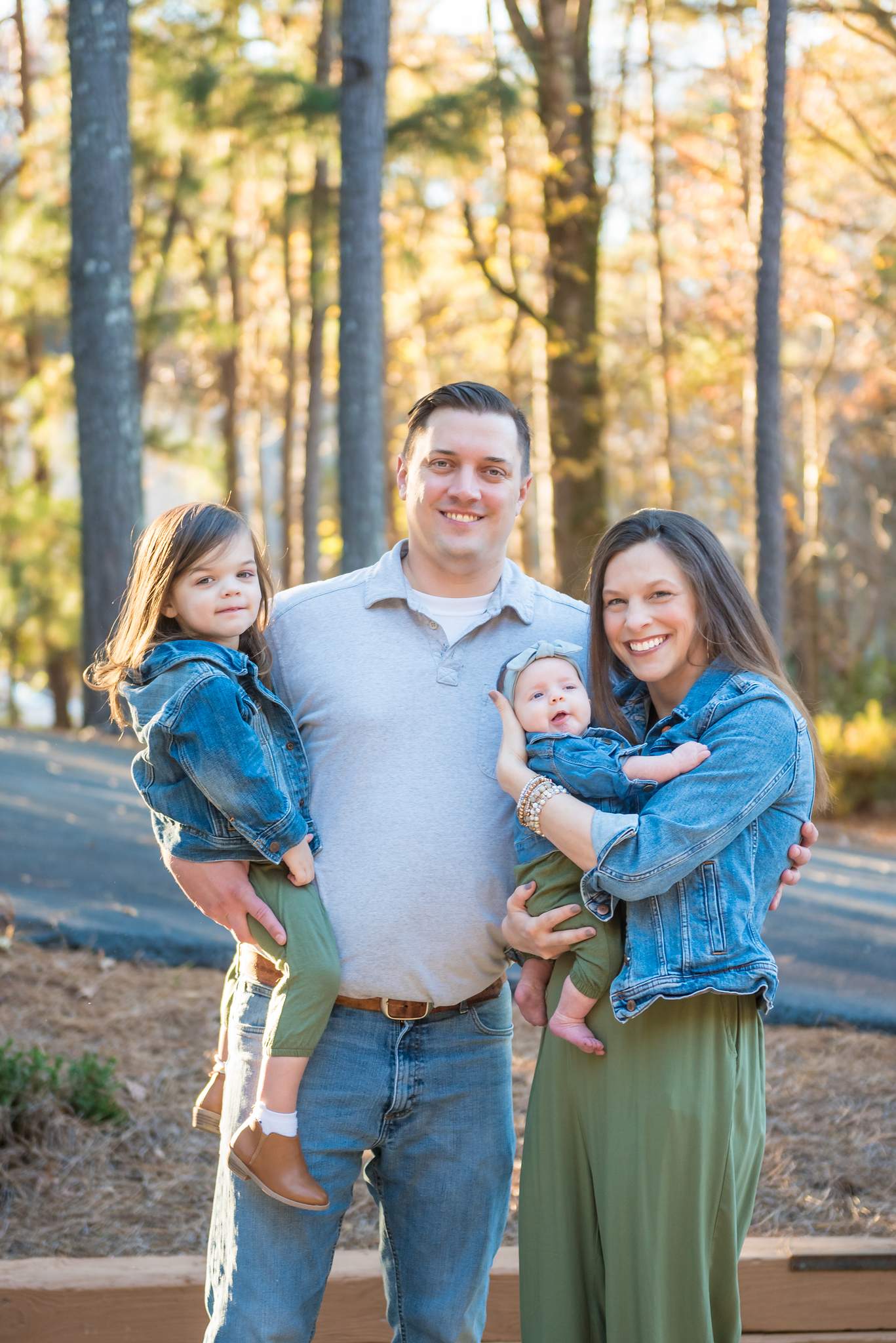 Dad in light jeans and a gray polo with mom and girls in denim jackets and olive green