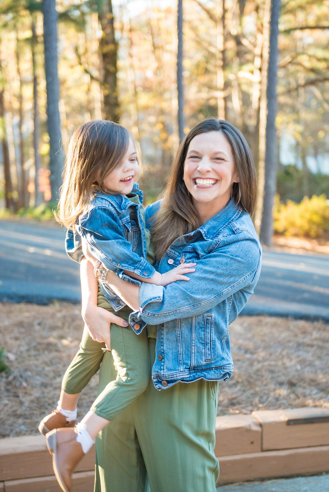Mom in a denim jacket and olive jumpsuit hugging her laughing toddler in coordinating denim and olive