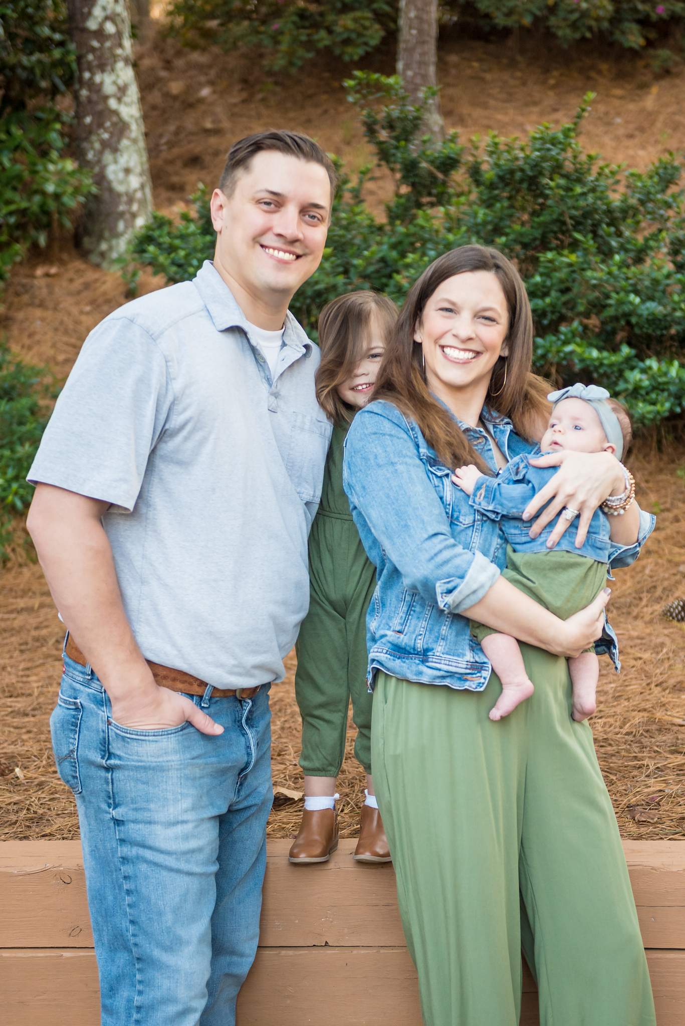Brown boots, light jeans, an olive jumpsuit and denim jackets on a family standing among pines