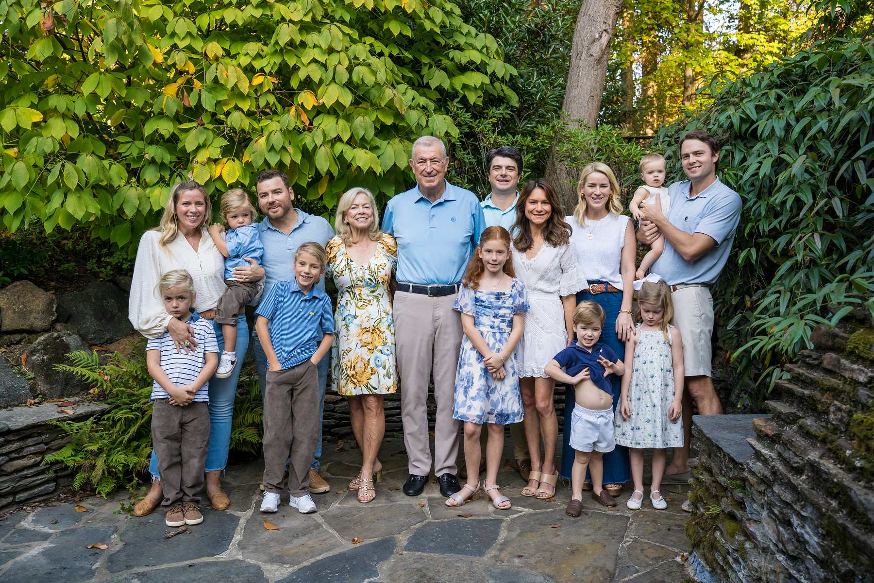 Extended family in blues, whites and yellow florals with kids in blue on a stone garden patio