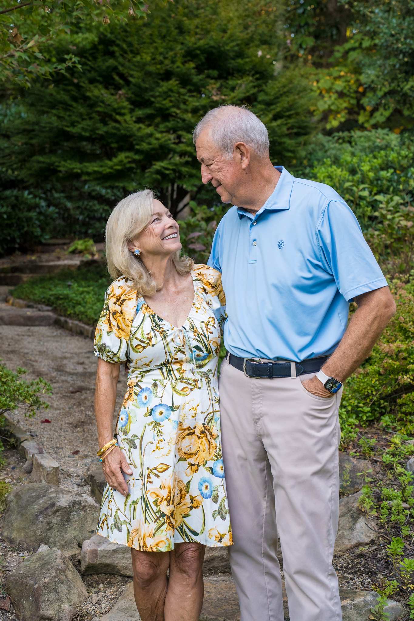 Couple in a yellow floral dress and a light blue polo with khakis smiling in a garden