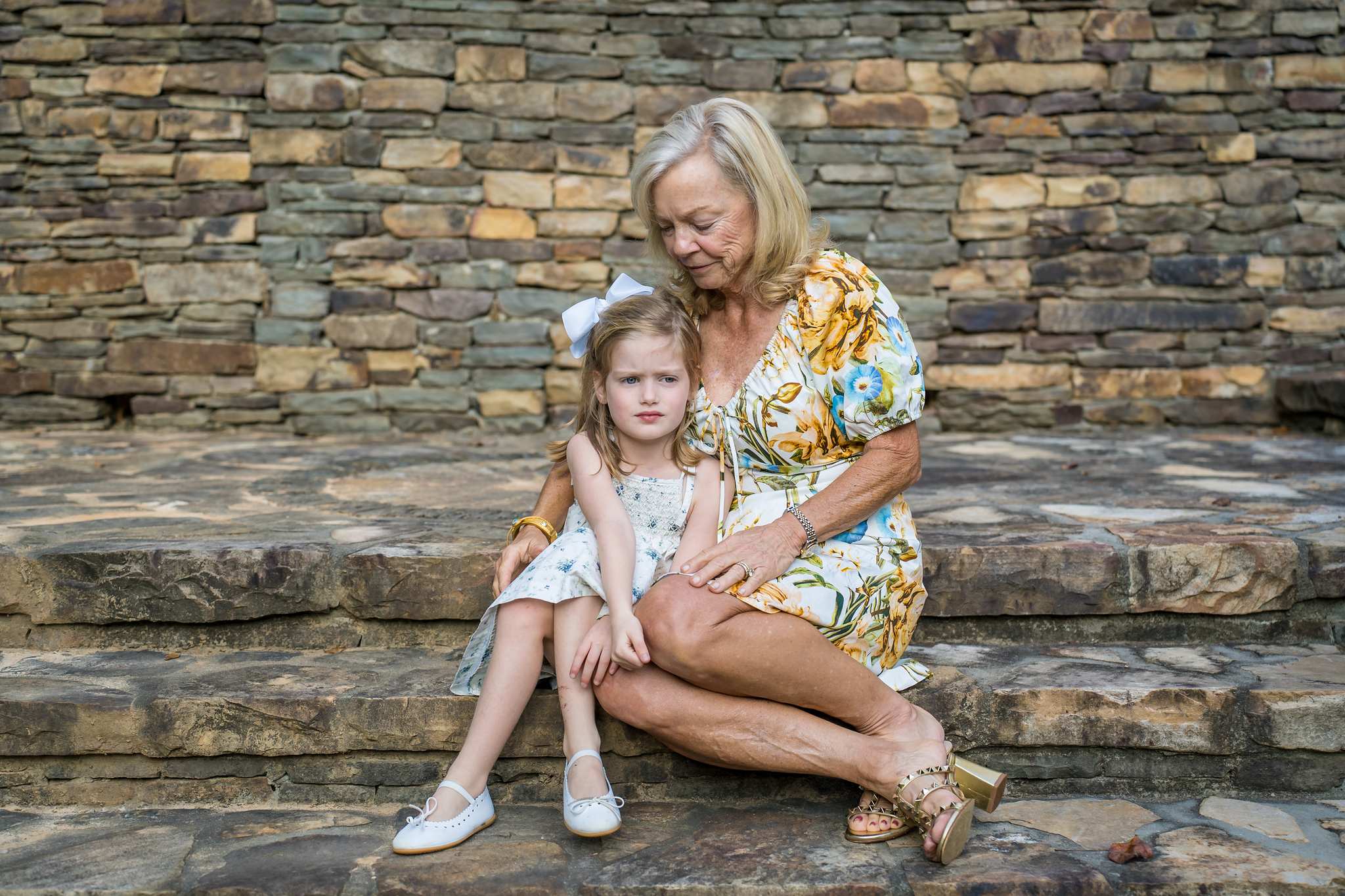 Woman in a yellow floral dress and a little girl in soft blue florals sitting on stone steps