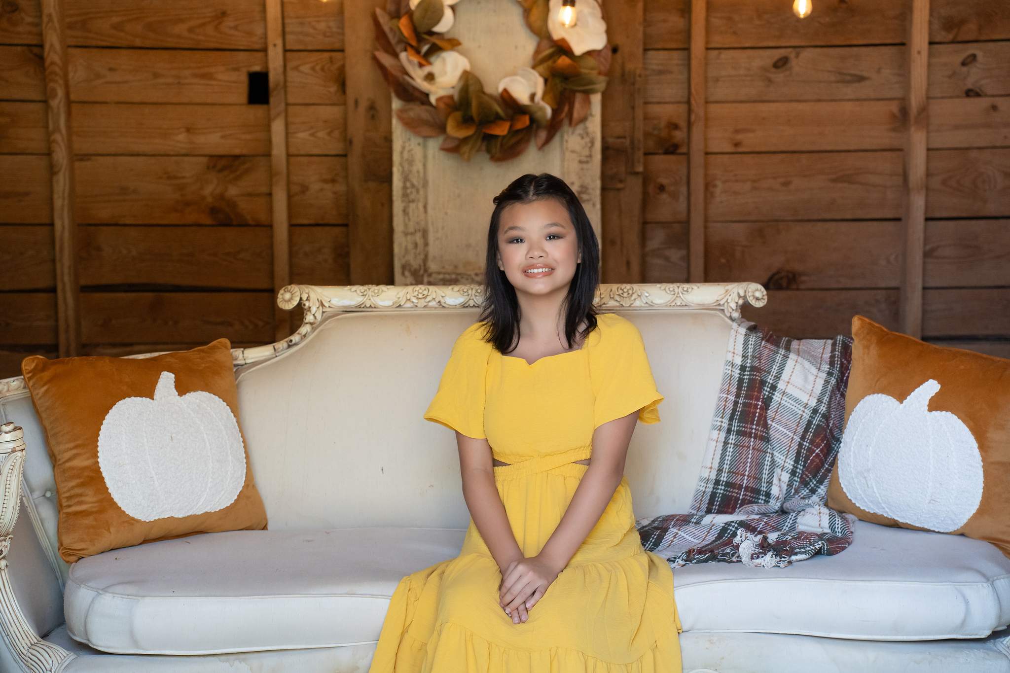 Girl in a mustard yellow dress on a white settee with pumpkin pillows at a fall mini session