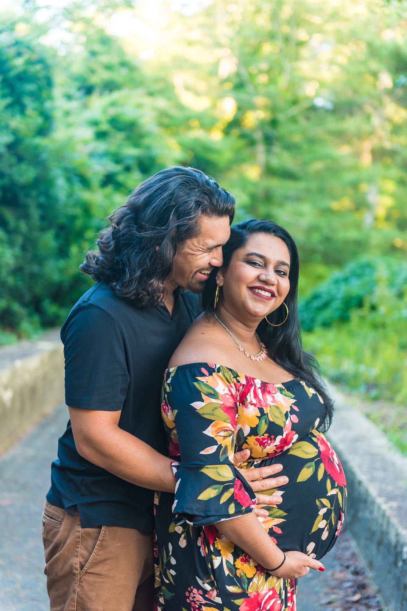Expecting mom in an off-shoulder navy floral dress, partner in a dark shirt and tan chinos