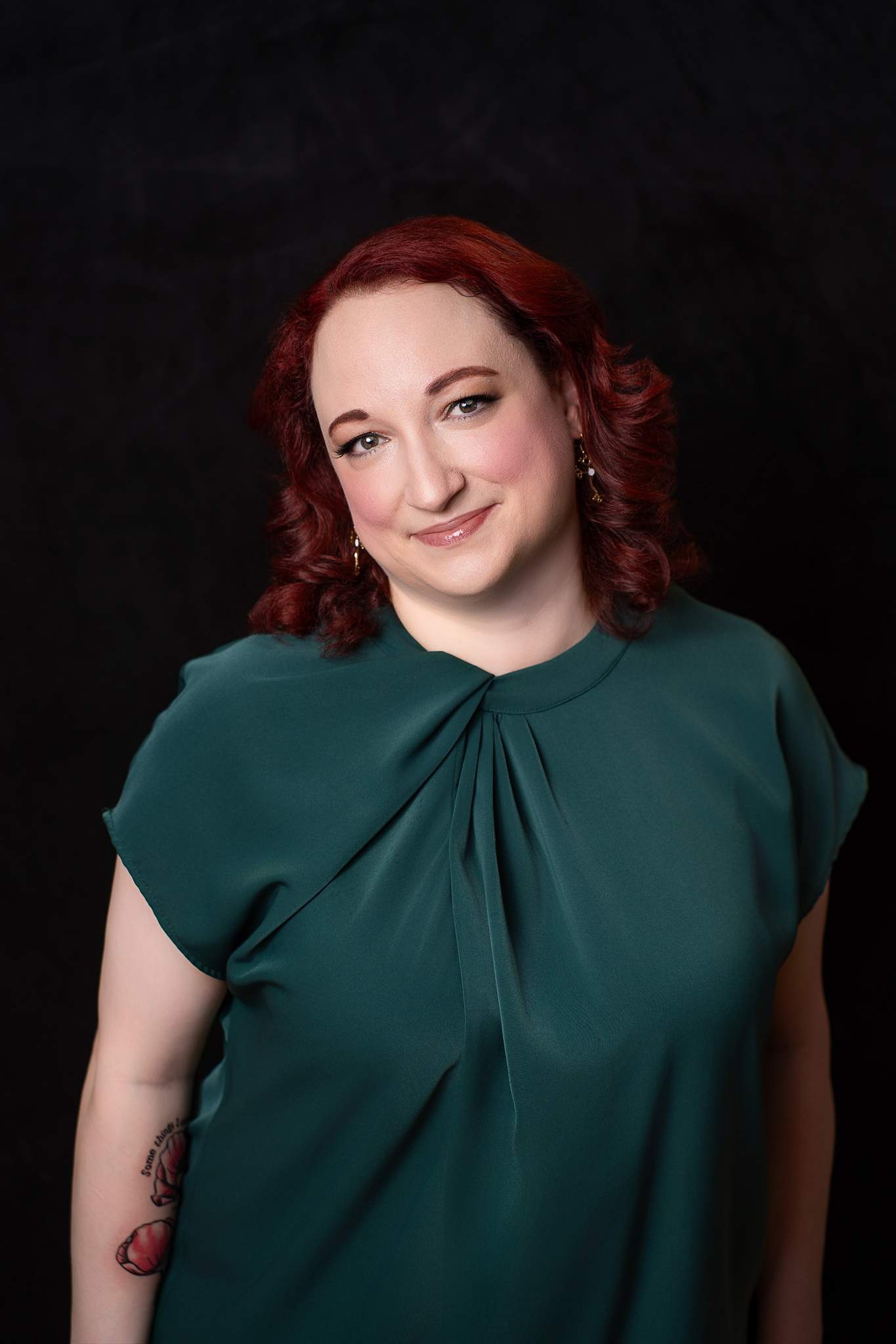 Headshot of a woman with red curls in an emerald green top on a black backdrop