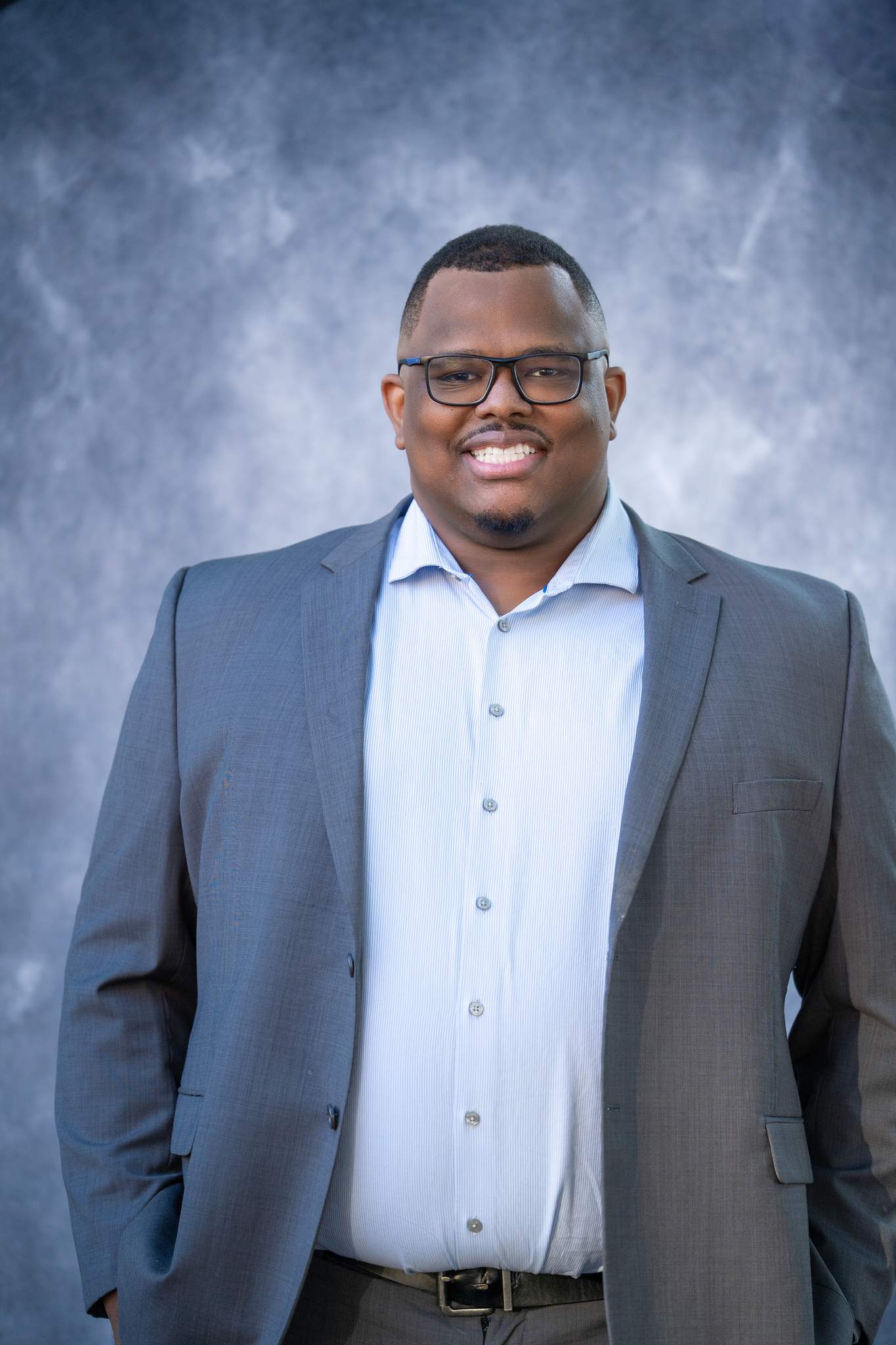 Business headshot of a man with glasses in a gray suit jacket over a light blue shirt