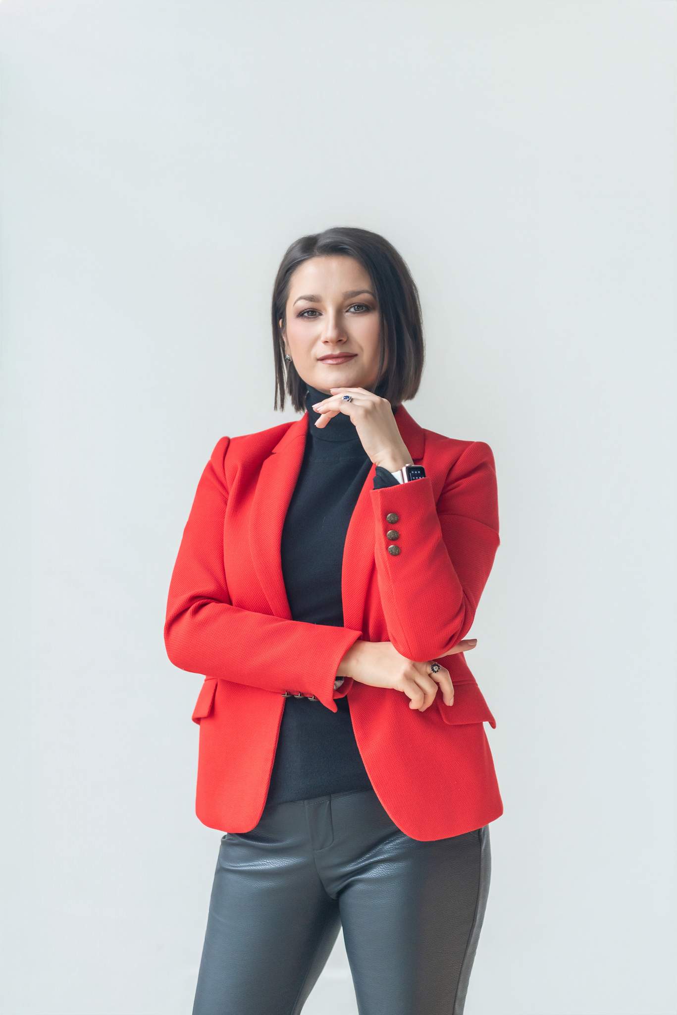 Woman in a red blazer over a black turtleneck against a light gray wall