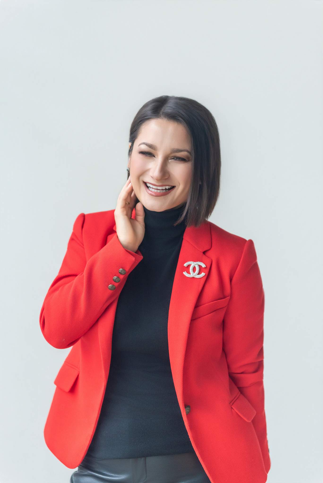 Smiling woman in a red blazer and black turtleneck with her hand at her chin