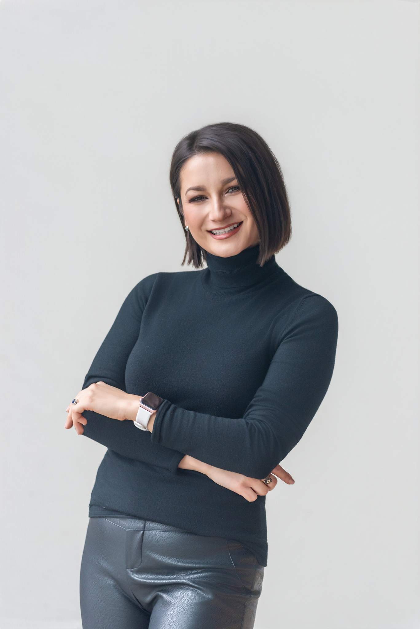 Smiling woman in a black turtleneck with arms crossed against a light gray wall